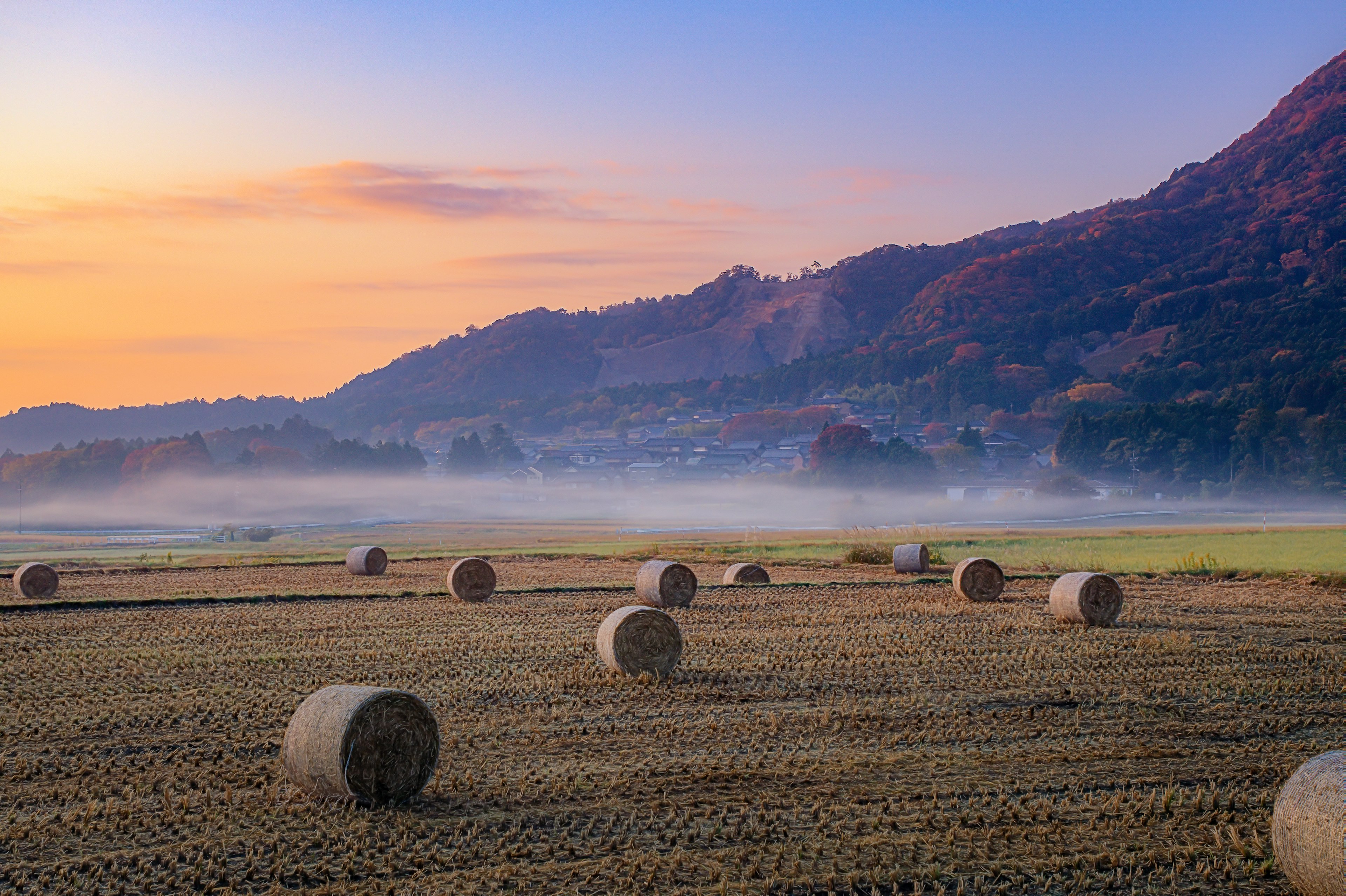 Heuballen auf einem Feld unter einem Sonnenuntergangshimmel mit entfernten Bergen