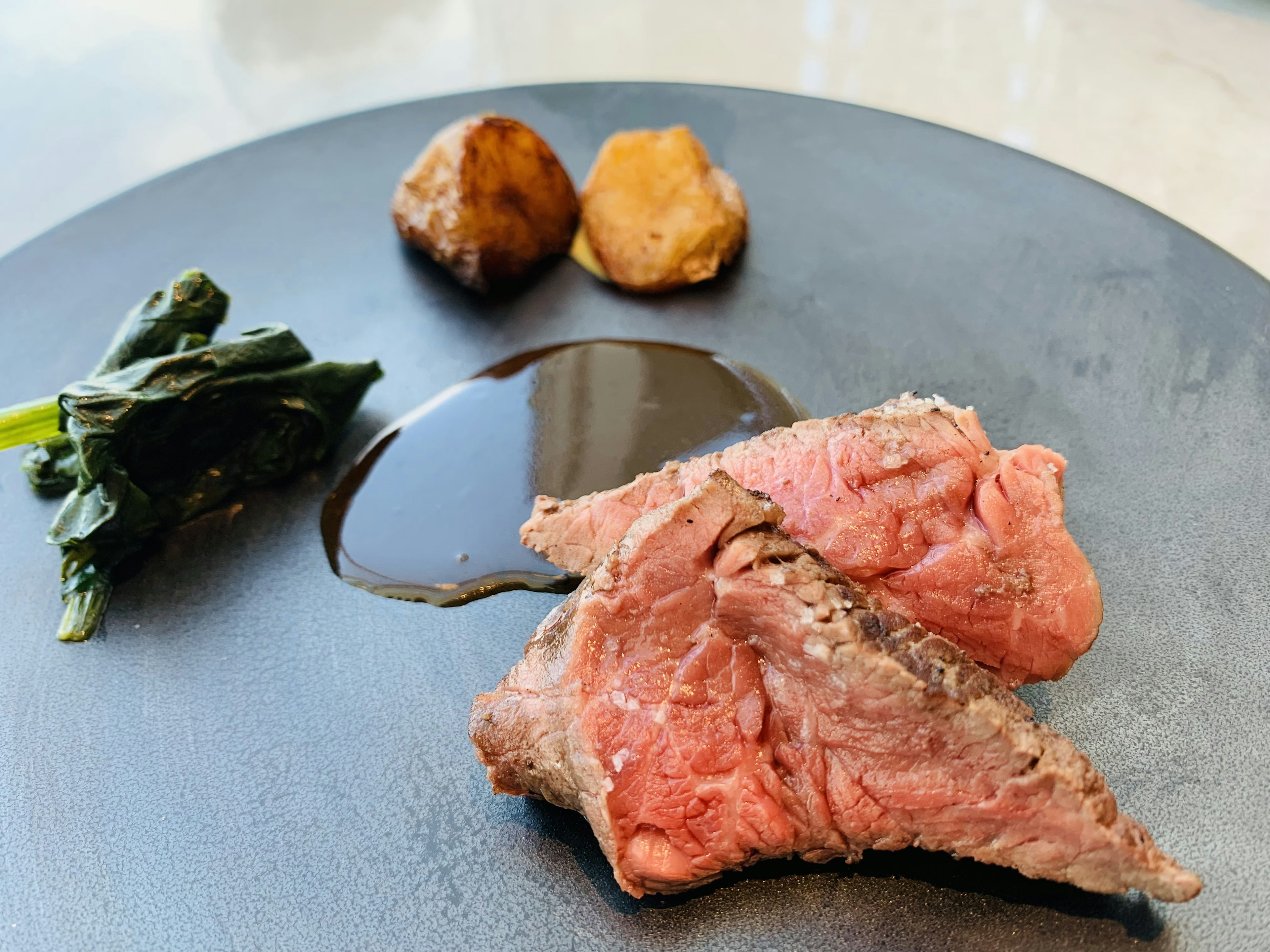 Boeuf rôti servi sur une assiette noire avec des pommes de terre et des légumes verts