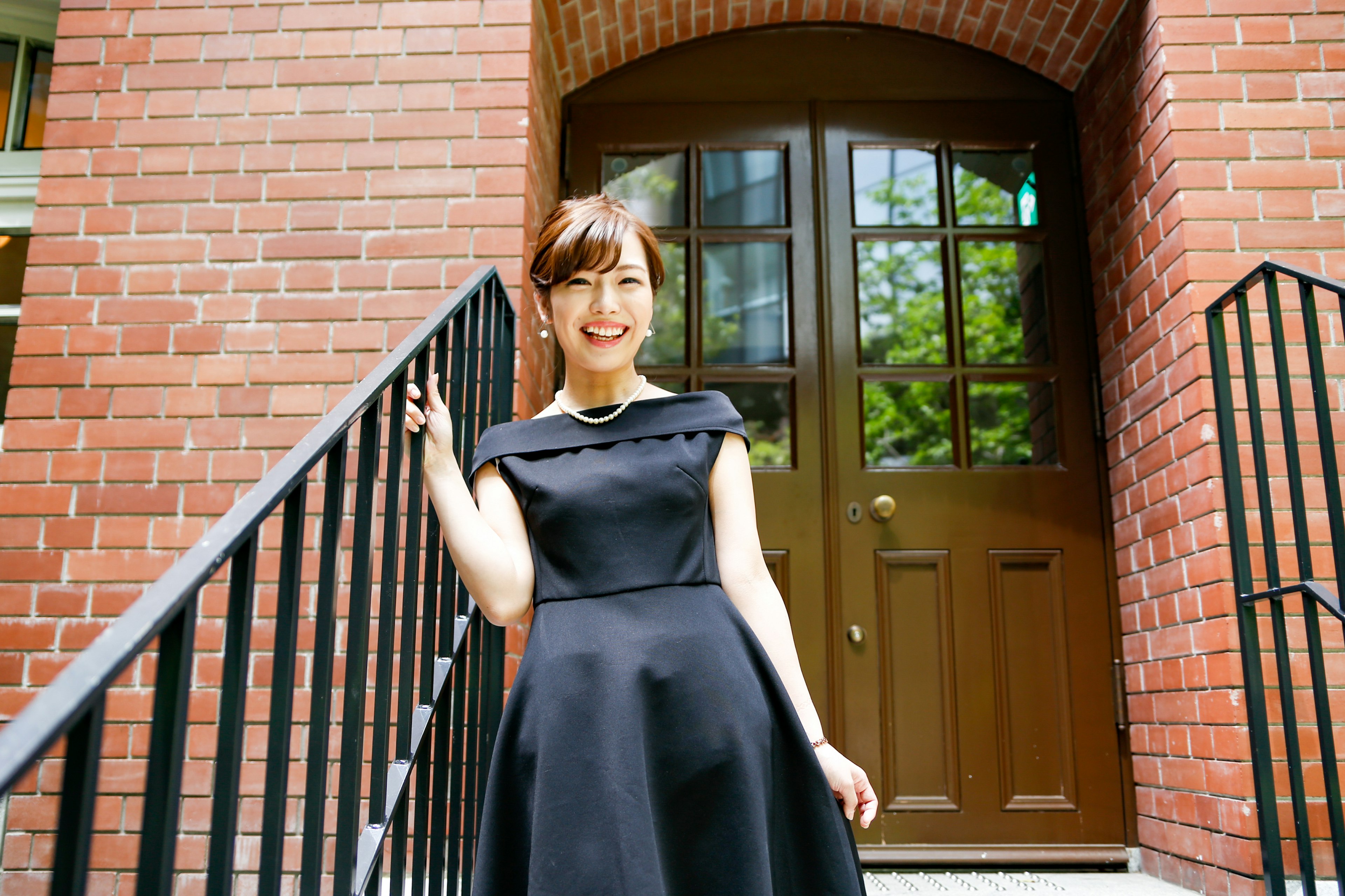 A woman in a black dress standing on stairs Bright lighting in front of a red brick building