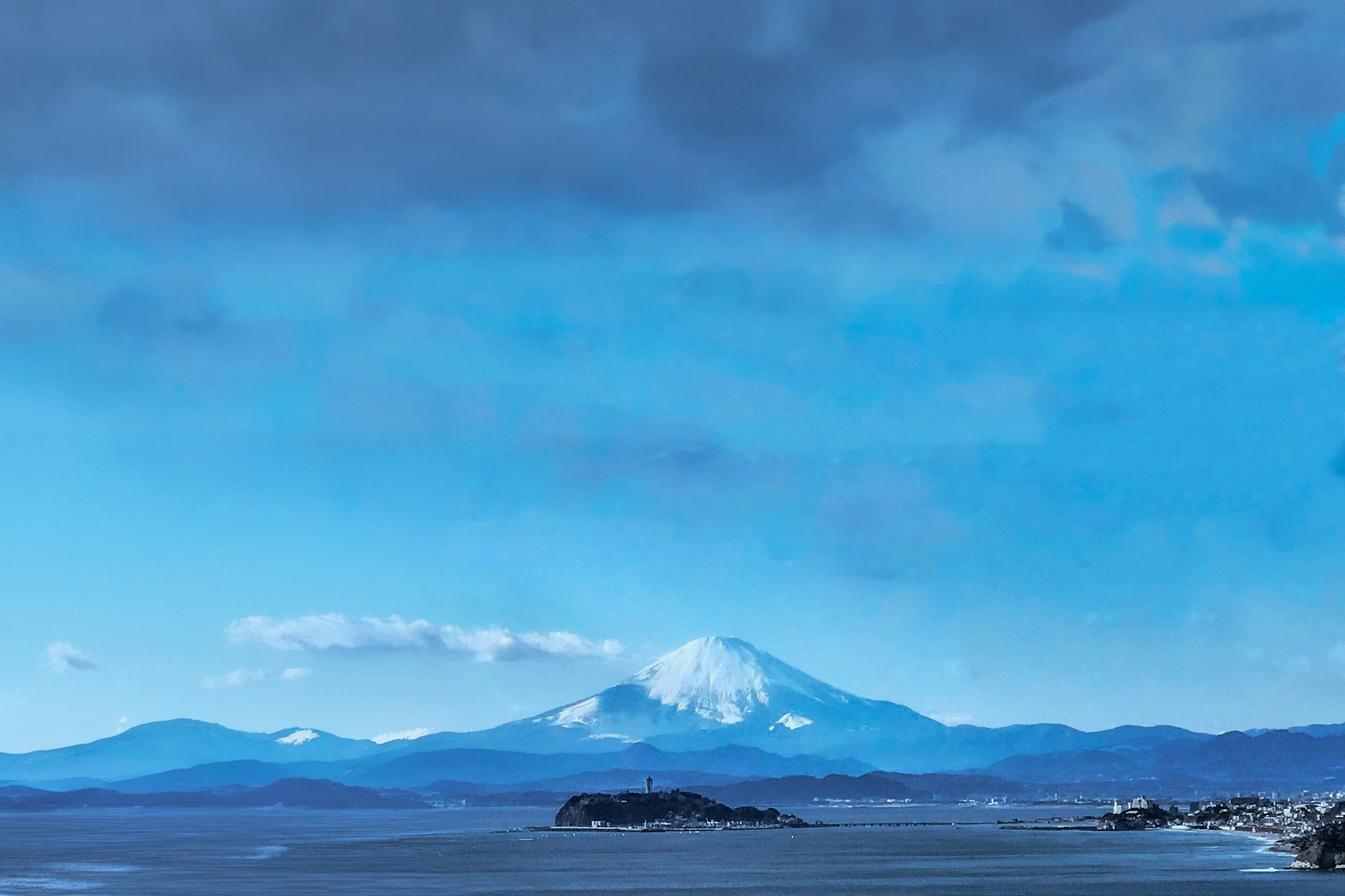 Panoramablick auf einen schneebedeckten Berg unter einem blauen Himmel mit einer nahegelegenen Insel und ruhiger See