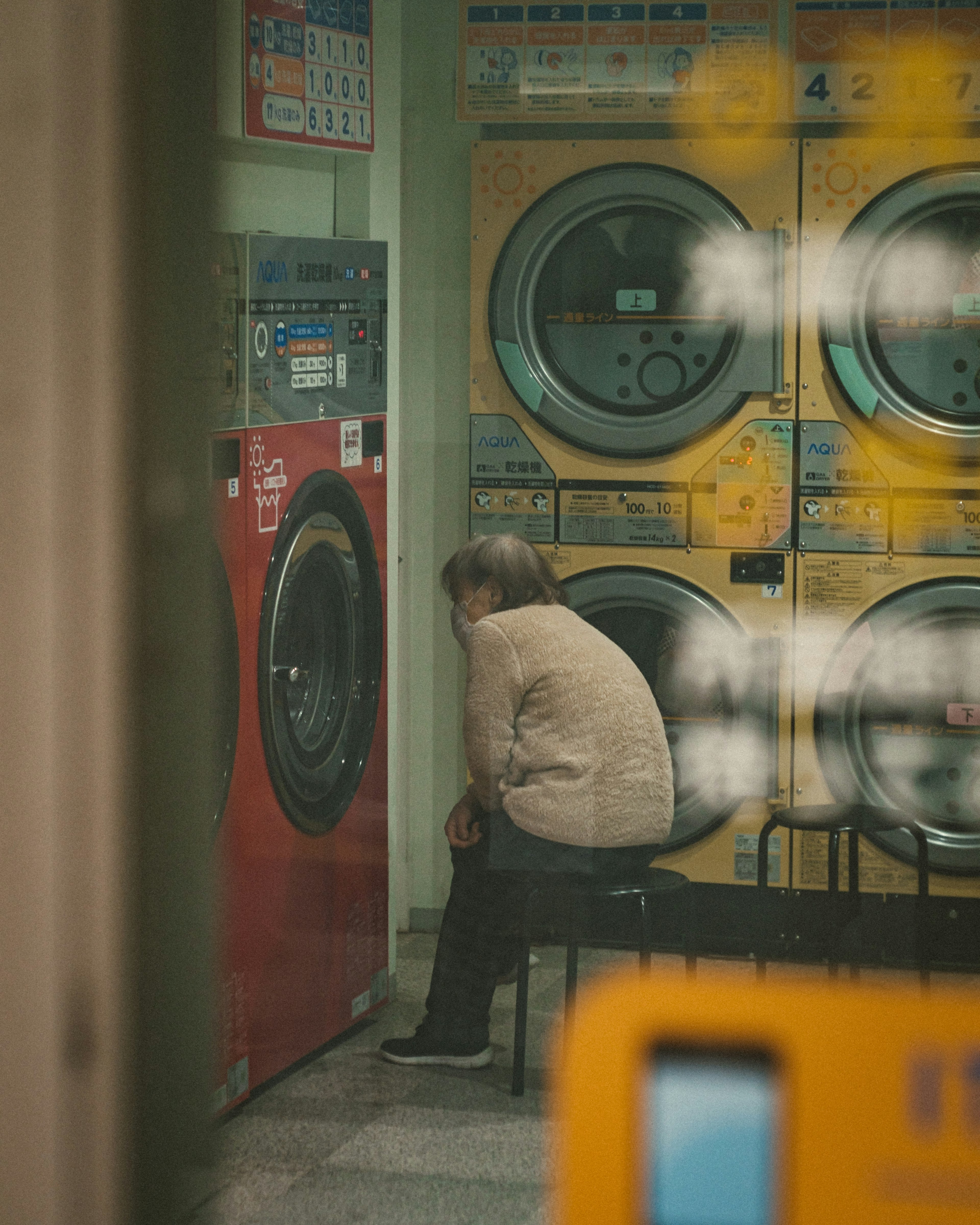 Une femme âgée assise devant une machine à laver machines colorées en arrière-plan