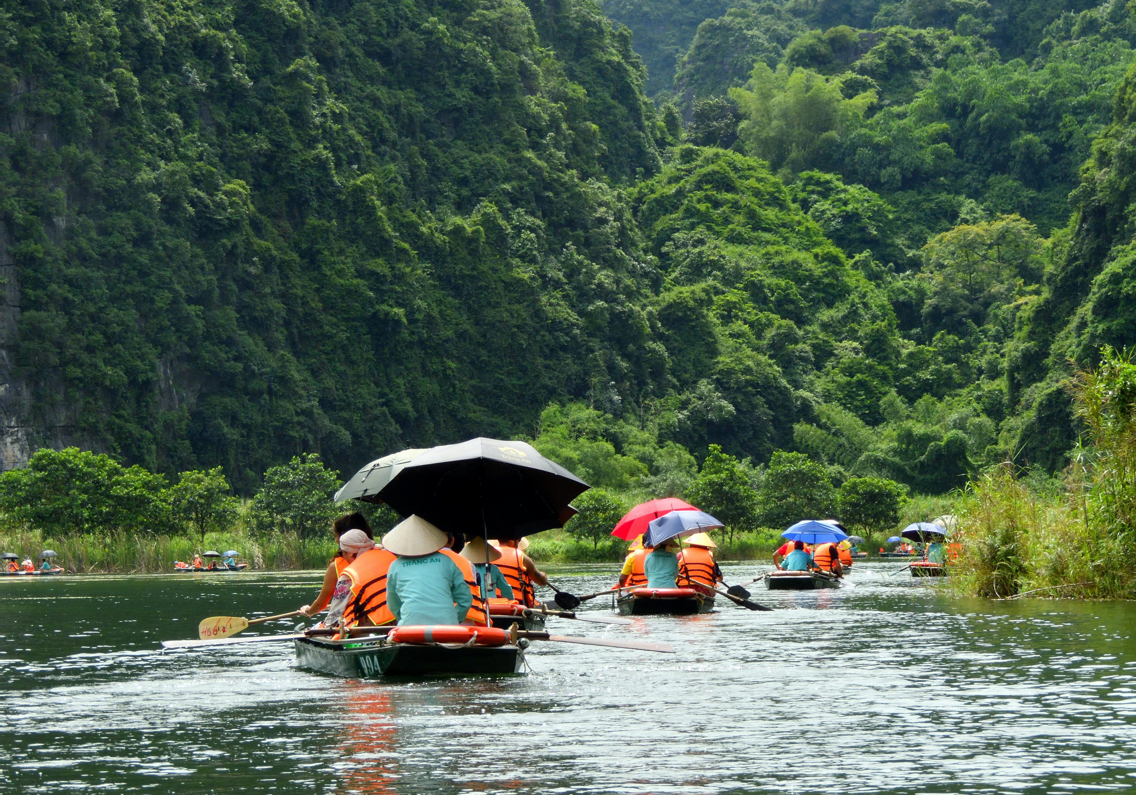 ผู้โดยสารพายเรือไปตามแม่น้ำที่เงียบสงบซึ่งล้อมรอบด้วยภูเขาที่เขียวขจี