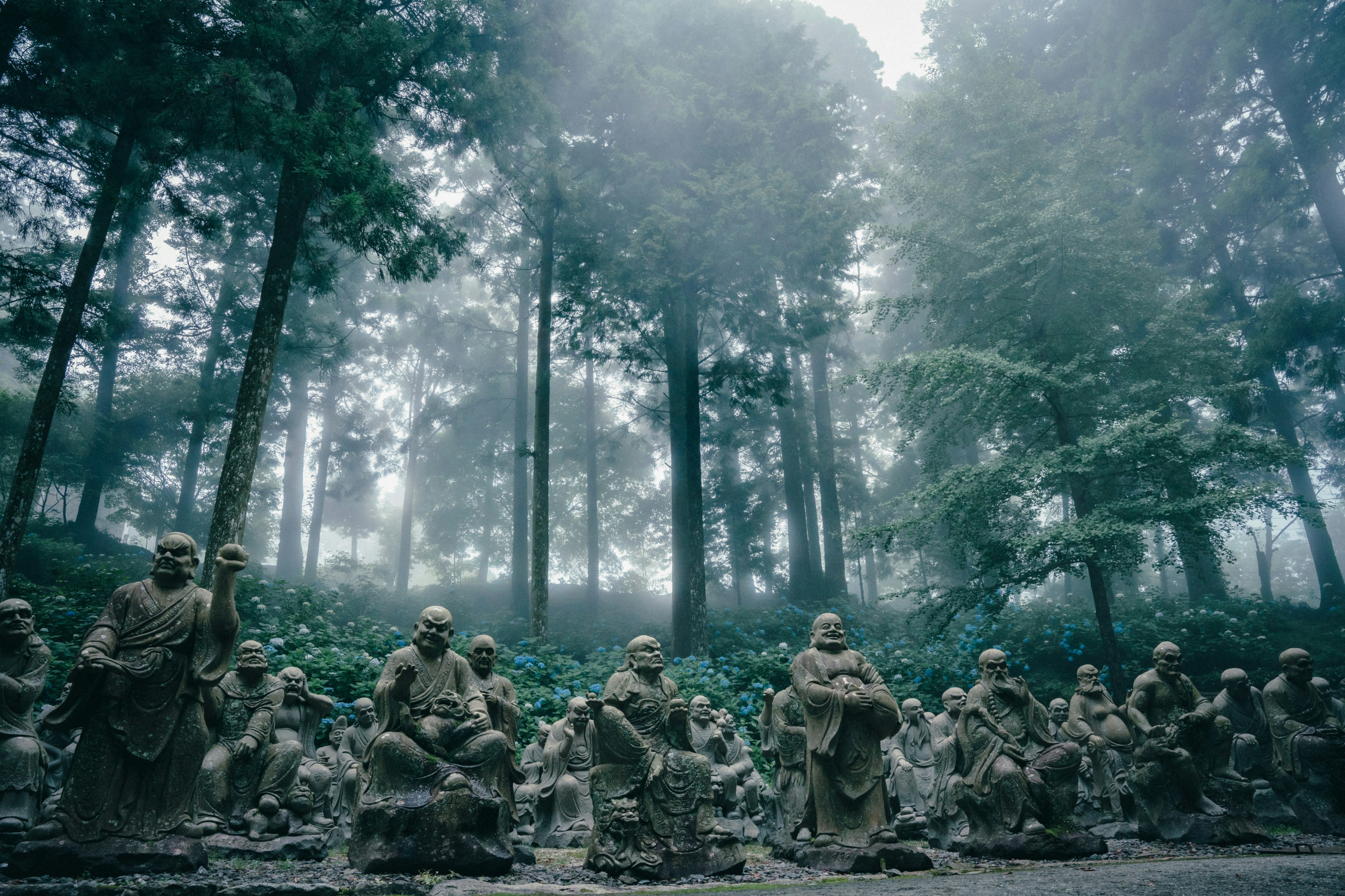 Eine Gruppe von Steinstatuen im Nebel mit hohen Bäumen im Hintergrund