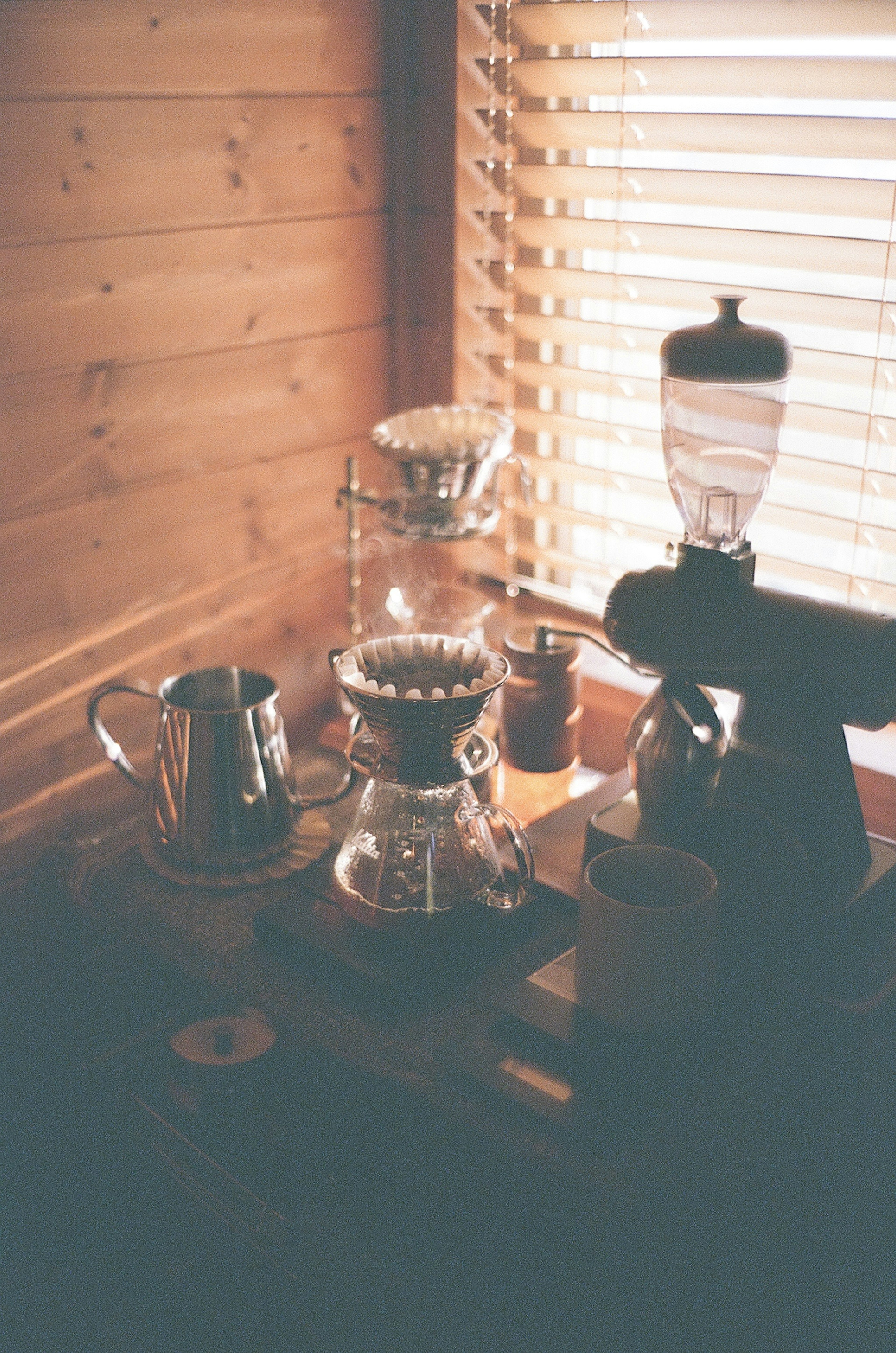 Coffee brewing setup featuring a grinder dripper and kettle near a wooden wall with blinds