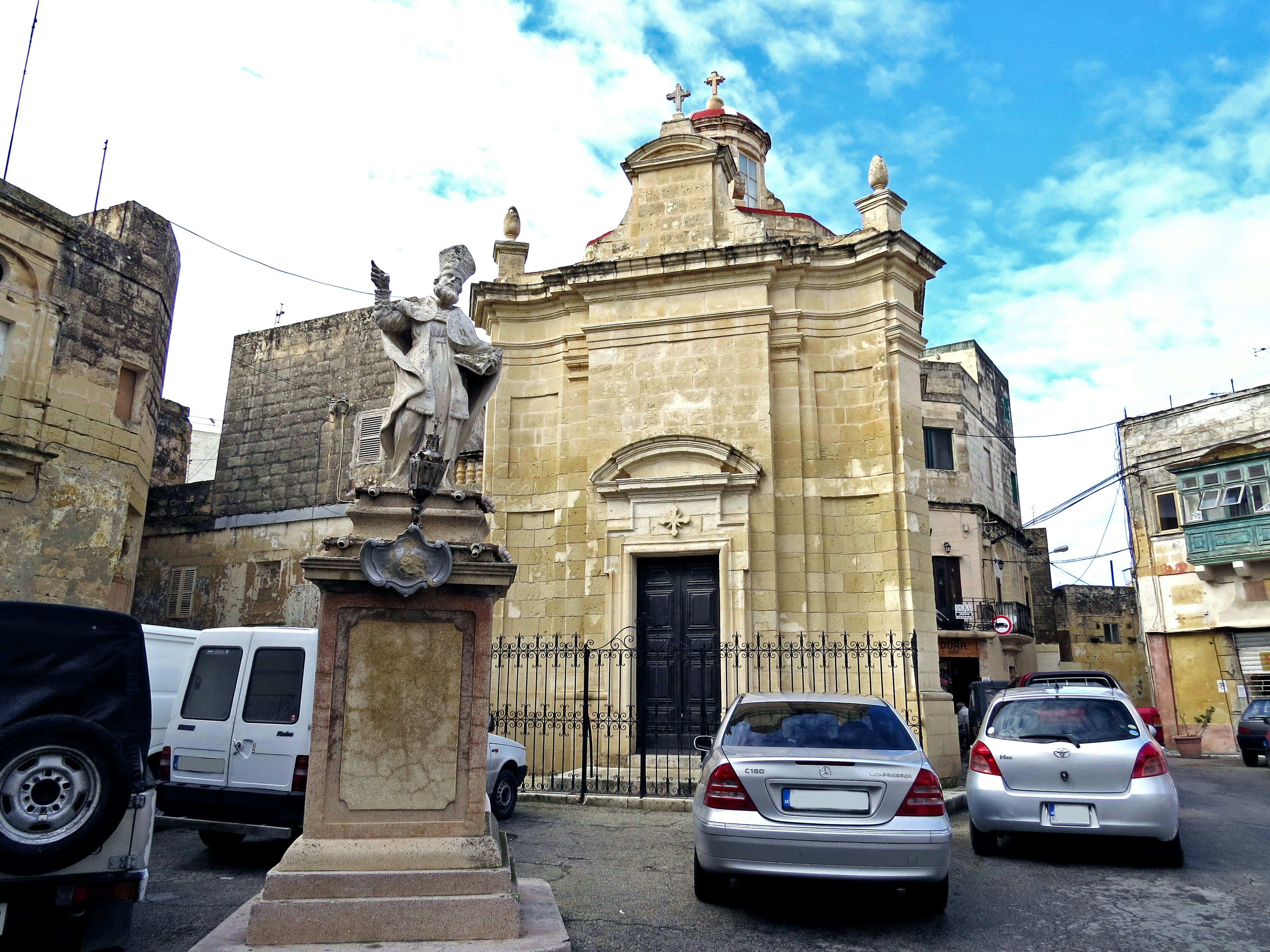 Une statue devant une église avec des voitures garées autour