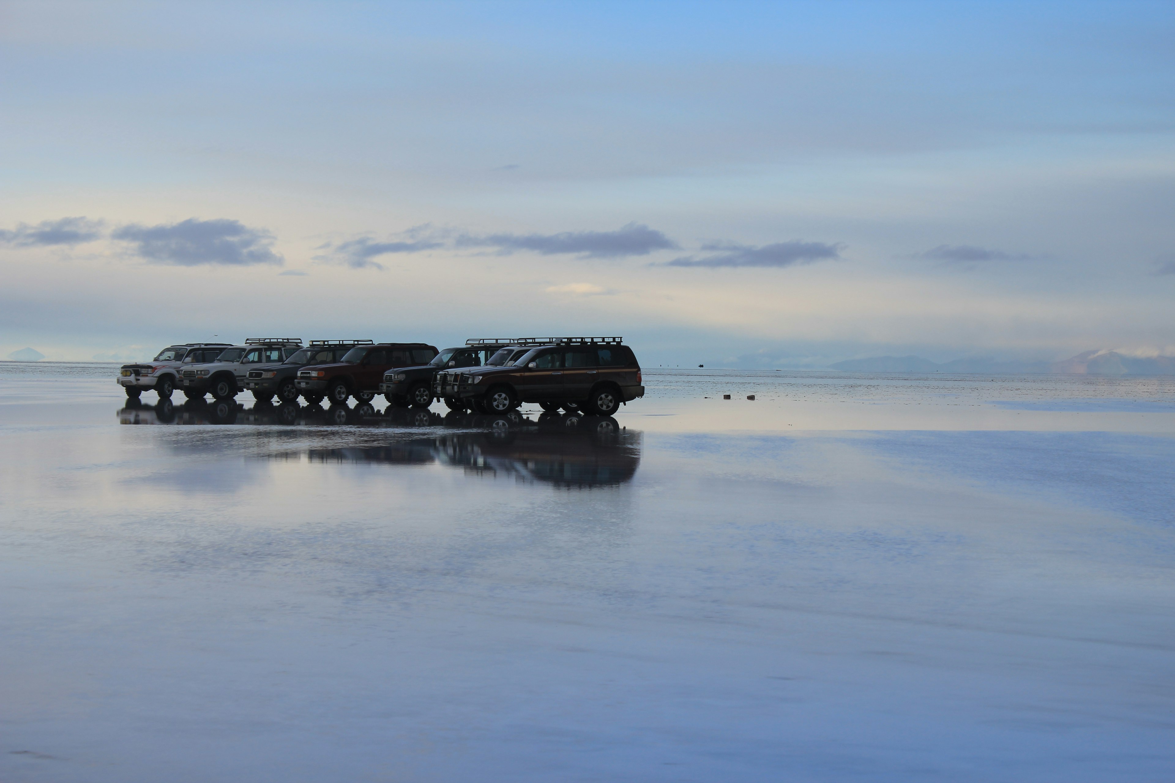 A group of vehicles reflected in the calm sea under a serene blue sky