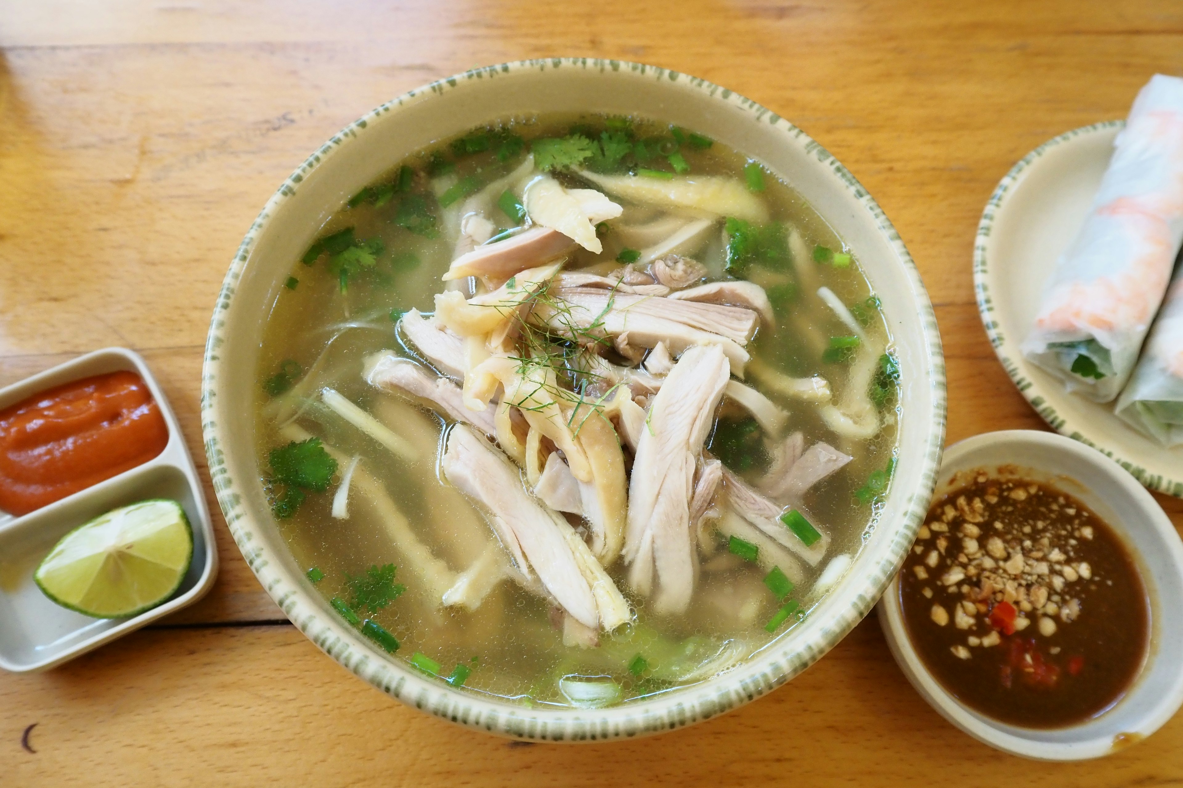 Bowl of chicken noodle soup with cilantro and lime, side sauces included