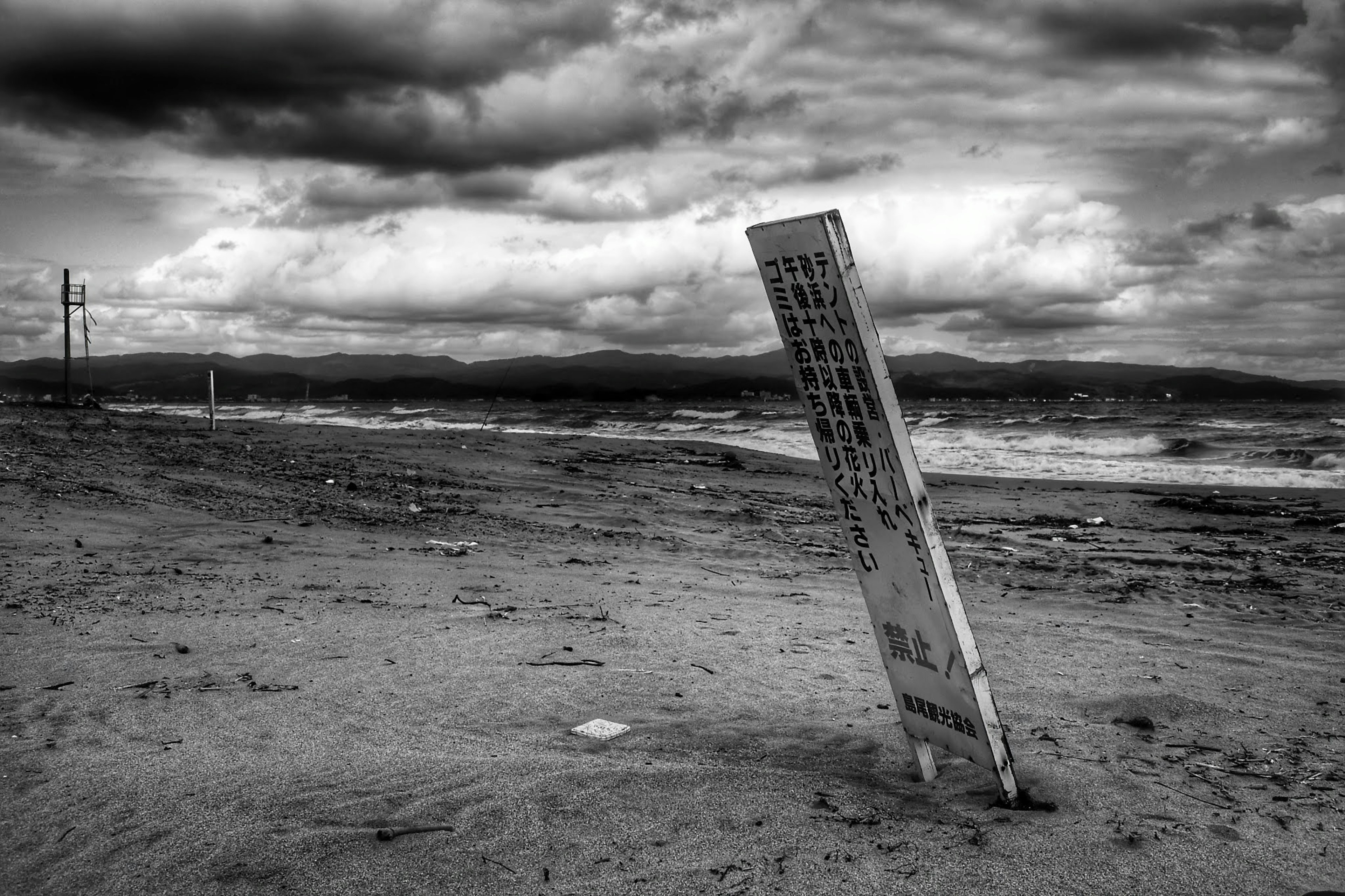 A white sign leaning on a desolate beach with dark clouds