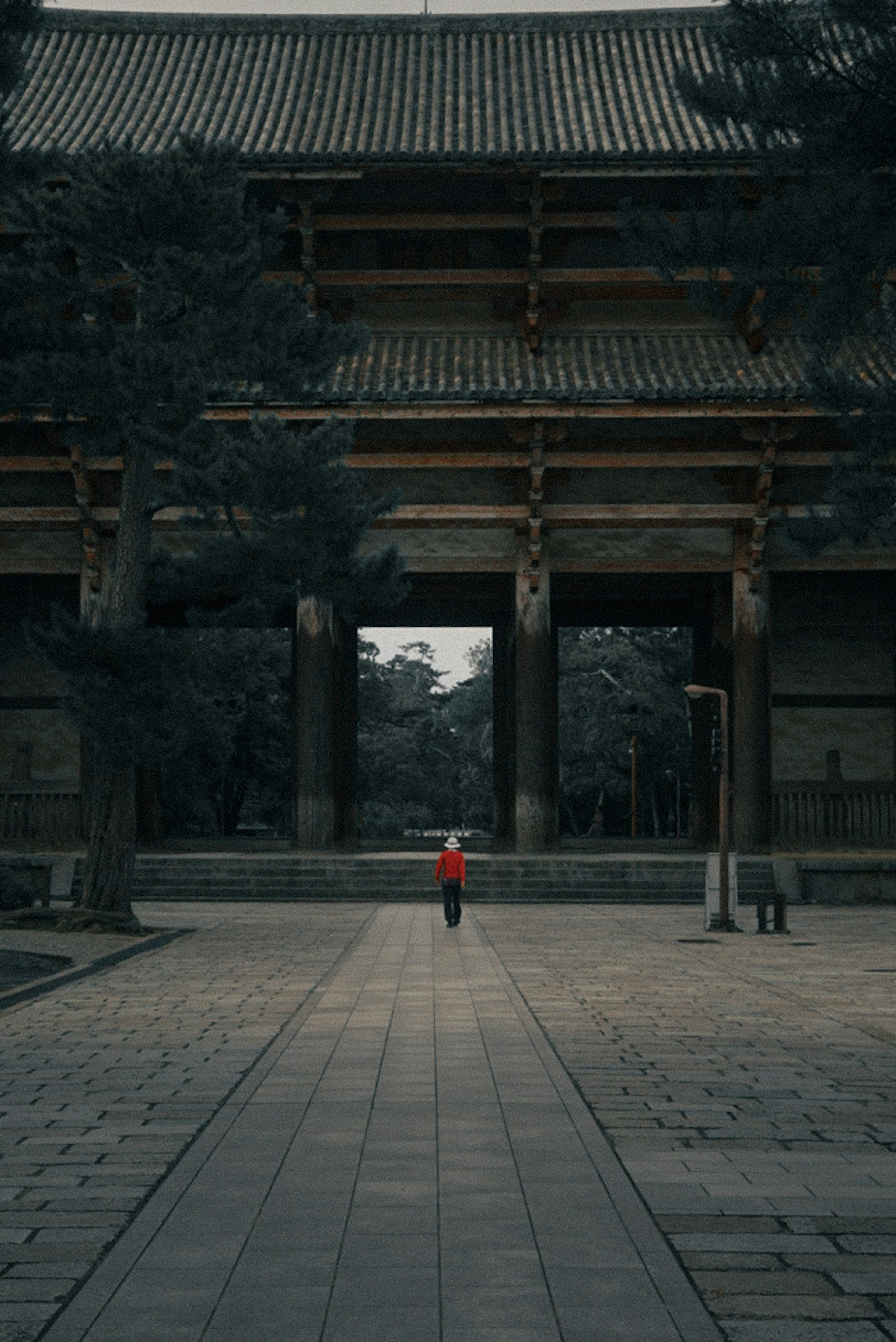 赤い服を着た人物が古い寺の前を歩いている