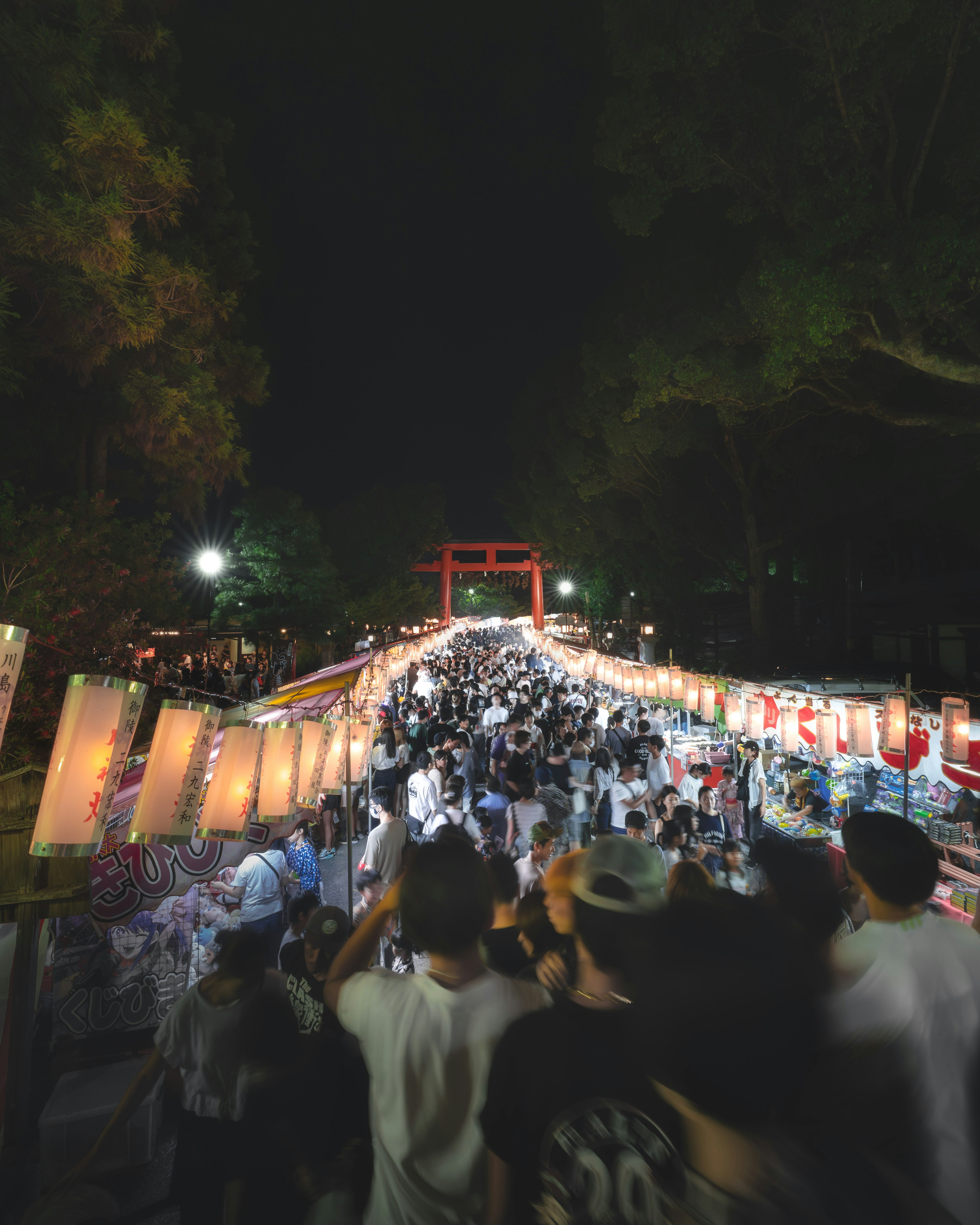 Multitud en un festival nocturno con faroles y una puerta torii