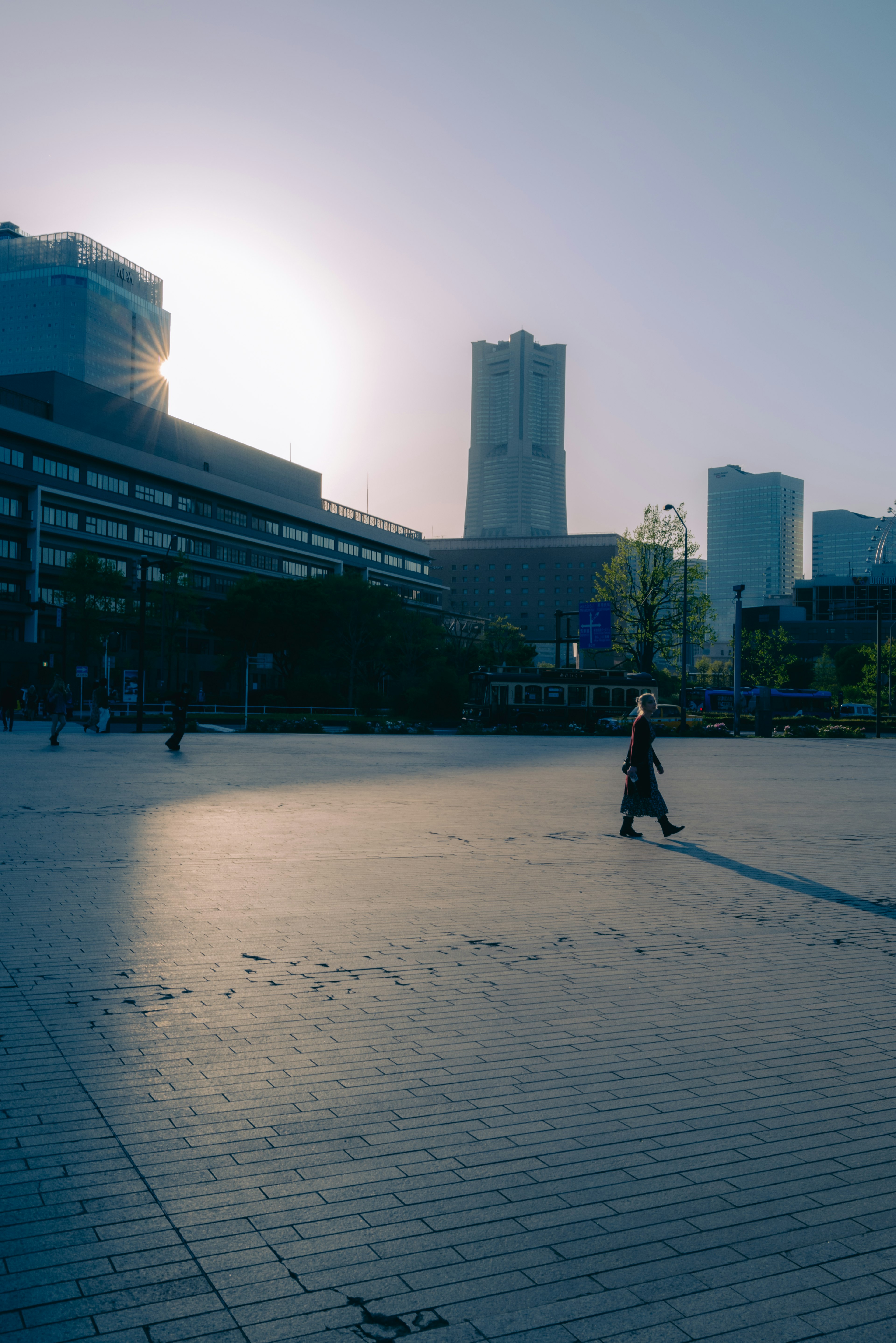 Woman walking in front of high-rise buildings with bright sunrise