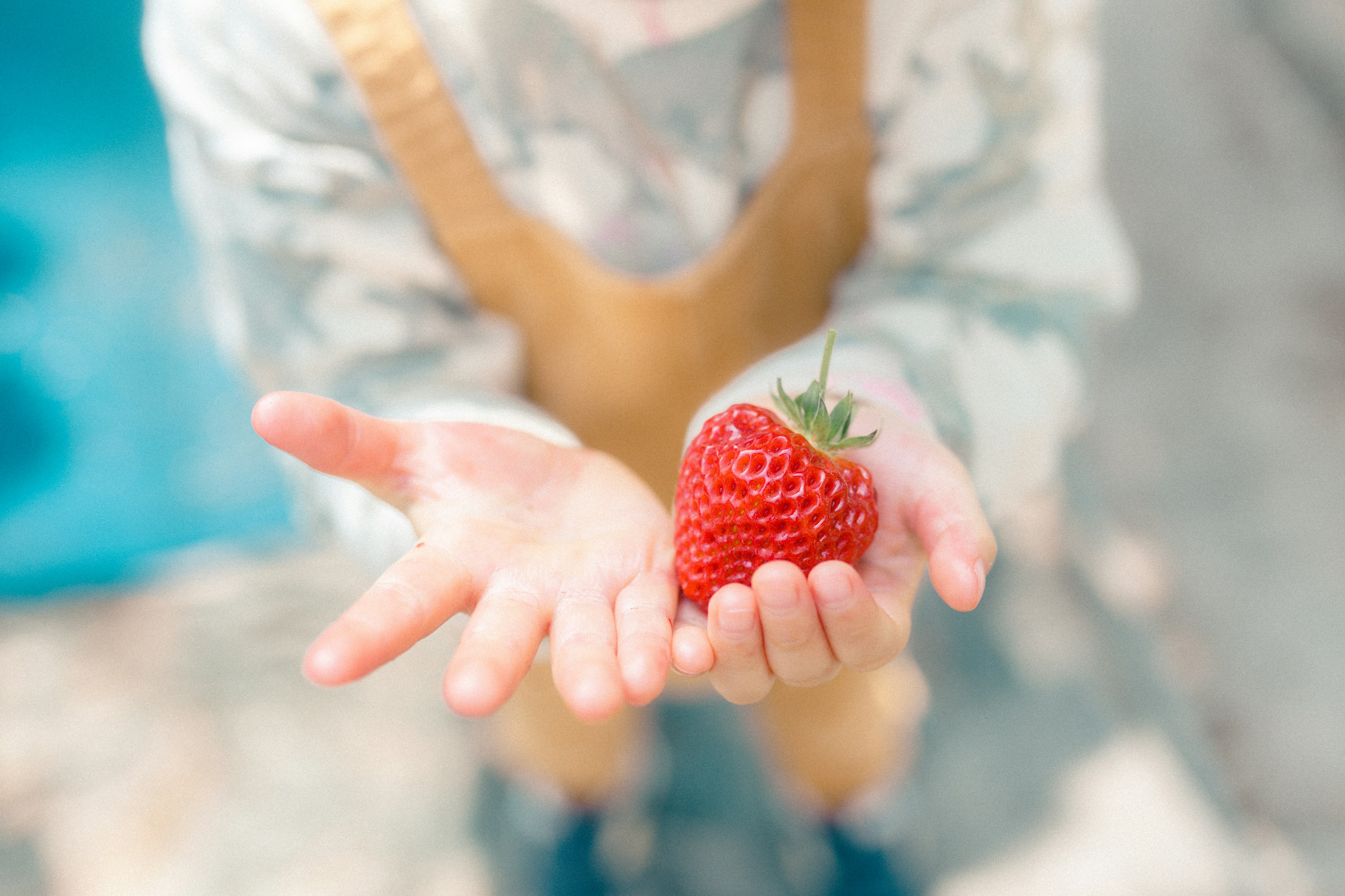 Bambino che tiene una grande fragola rossa tra le mani