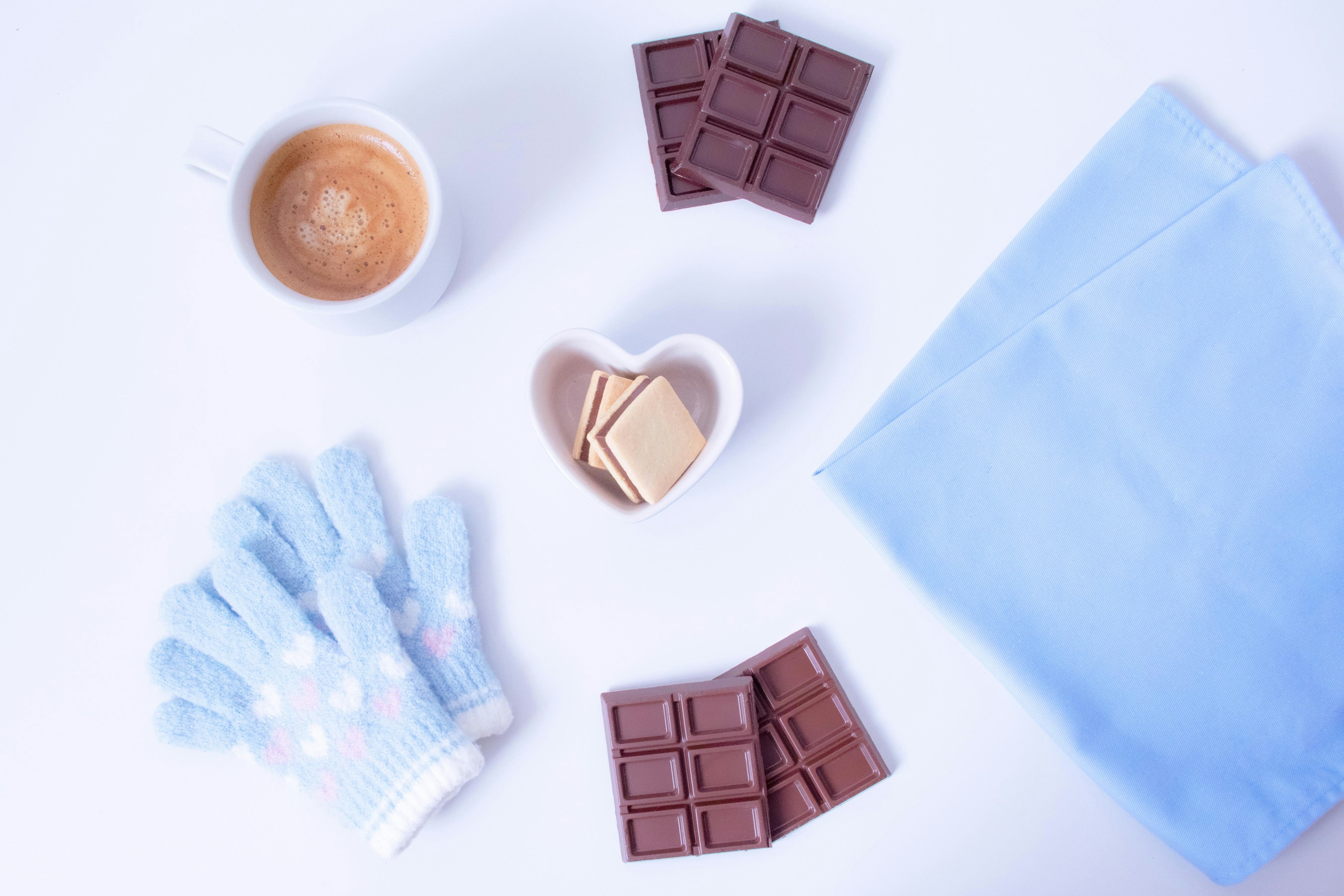 Escena que presenta café, chocolate, galletas y guantes sobre un paño azul