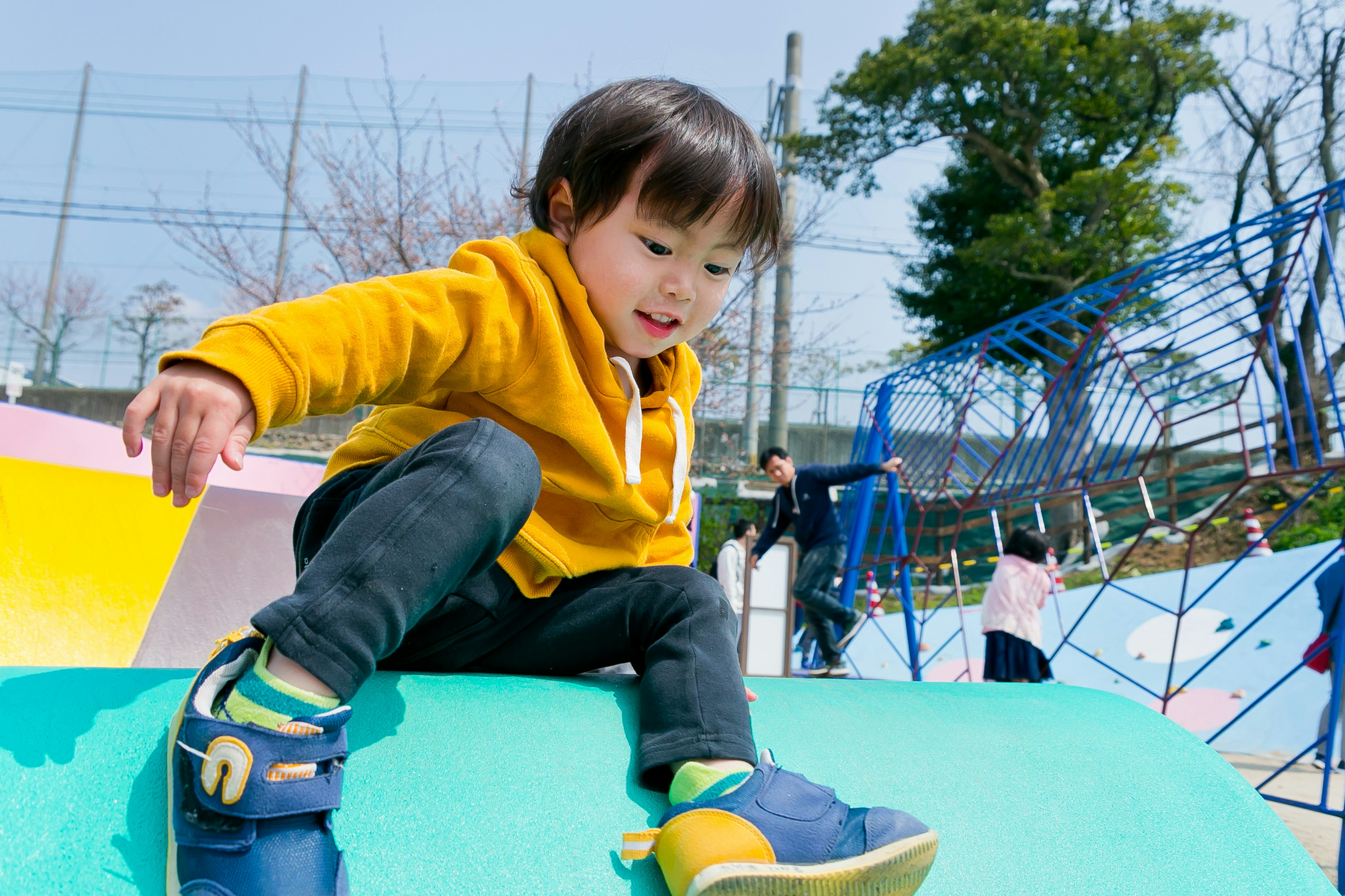 A child playing on playground equipment wearing a yellow hoodie