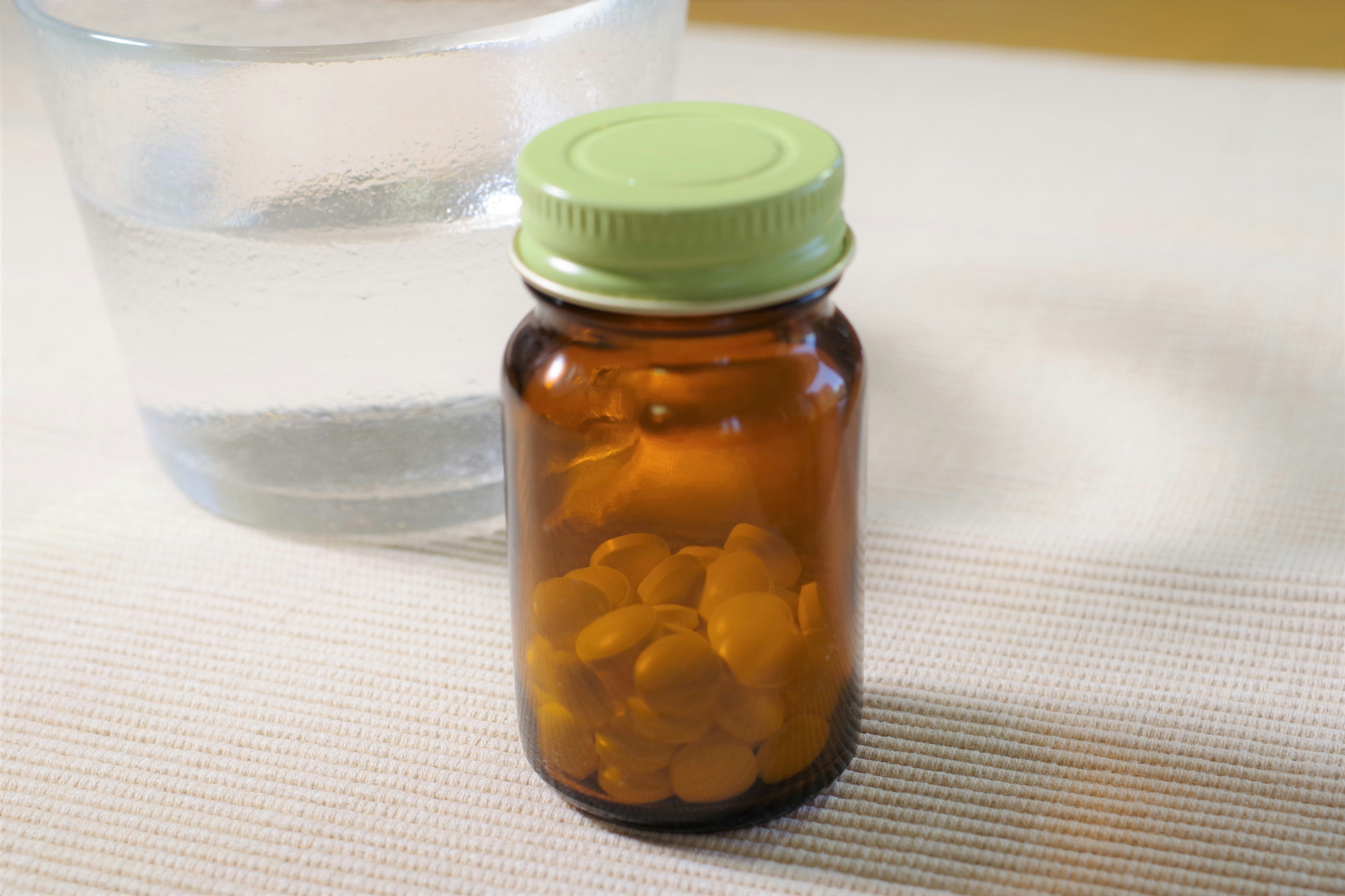 Brown bottle containing orange capsules next to a glass of water