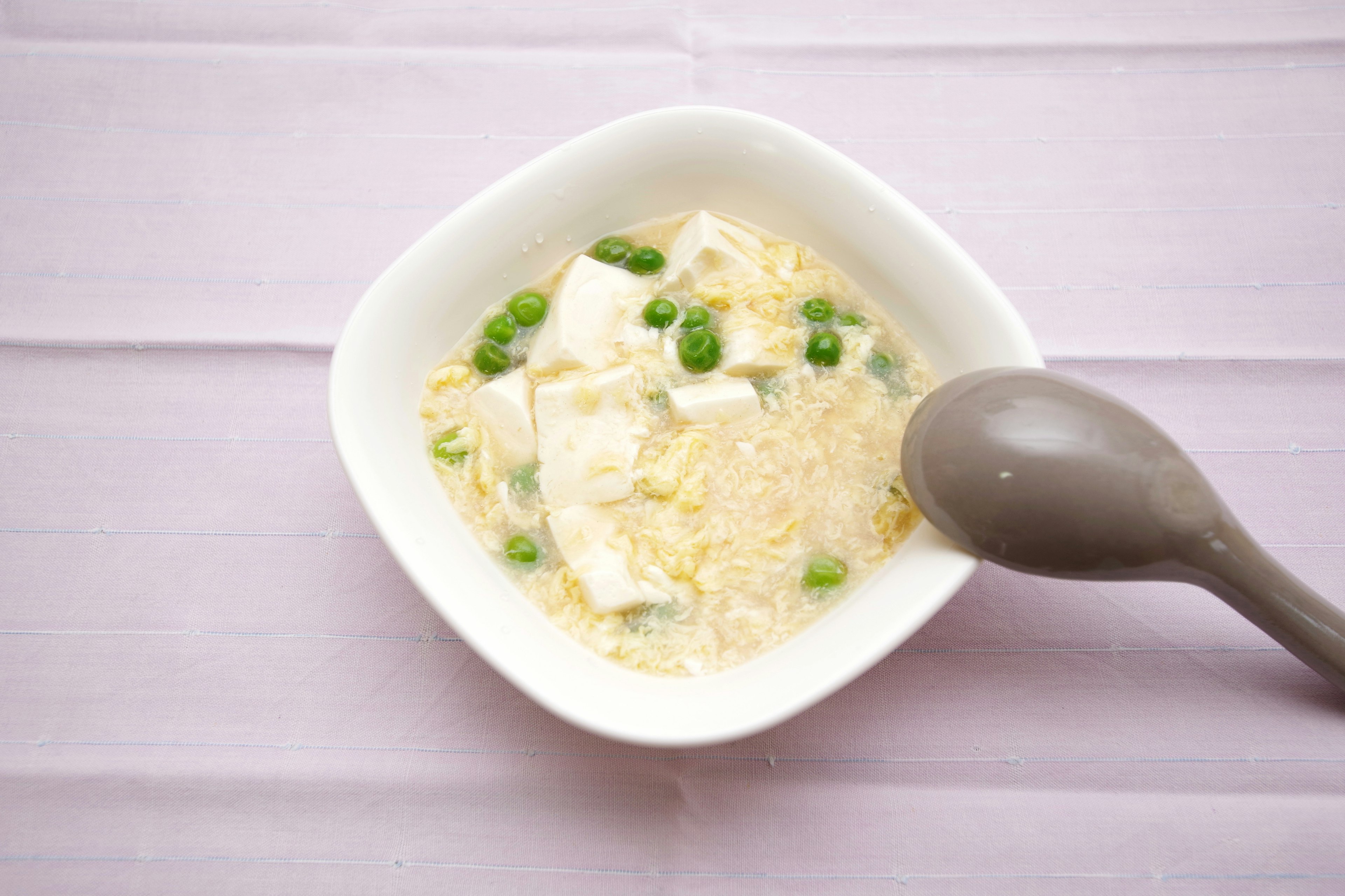 Zuppa di uova e tofu in una ciotola bianca con piselli verdi