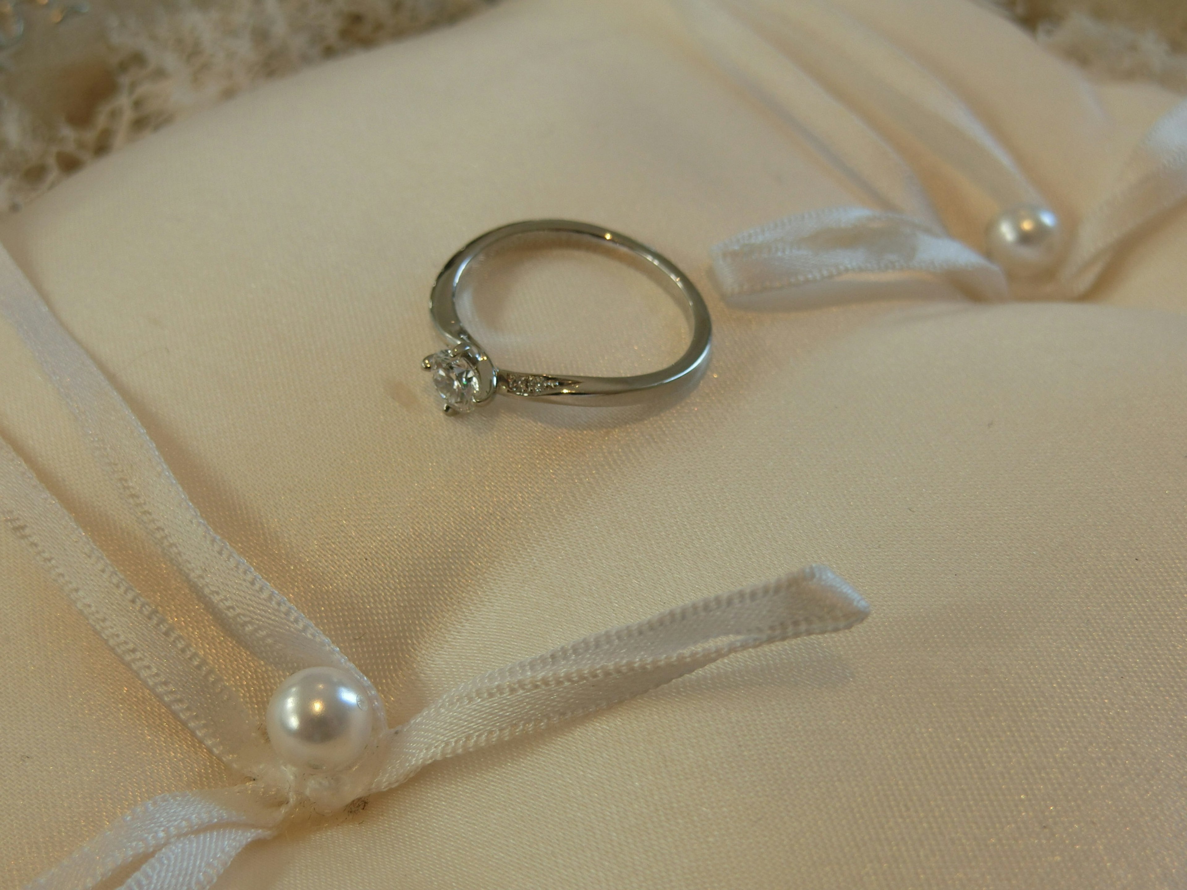 Diamond ring resting on a cream-colored cushion with pearl accents