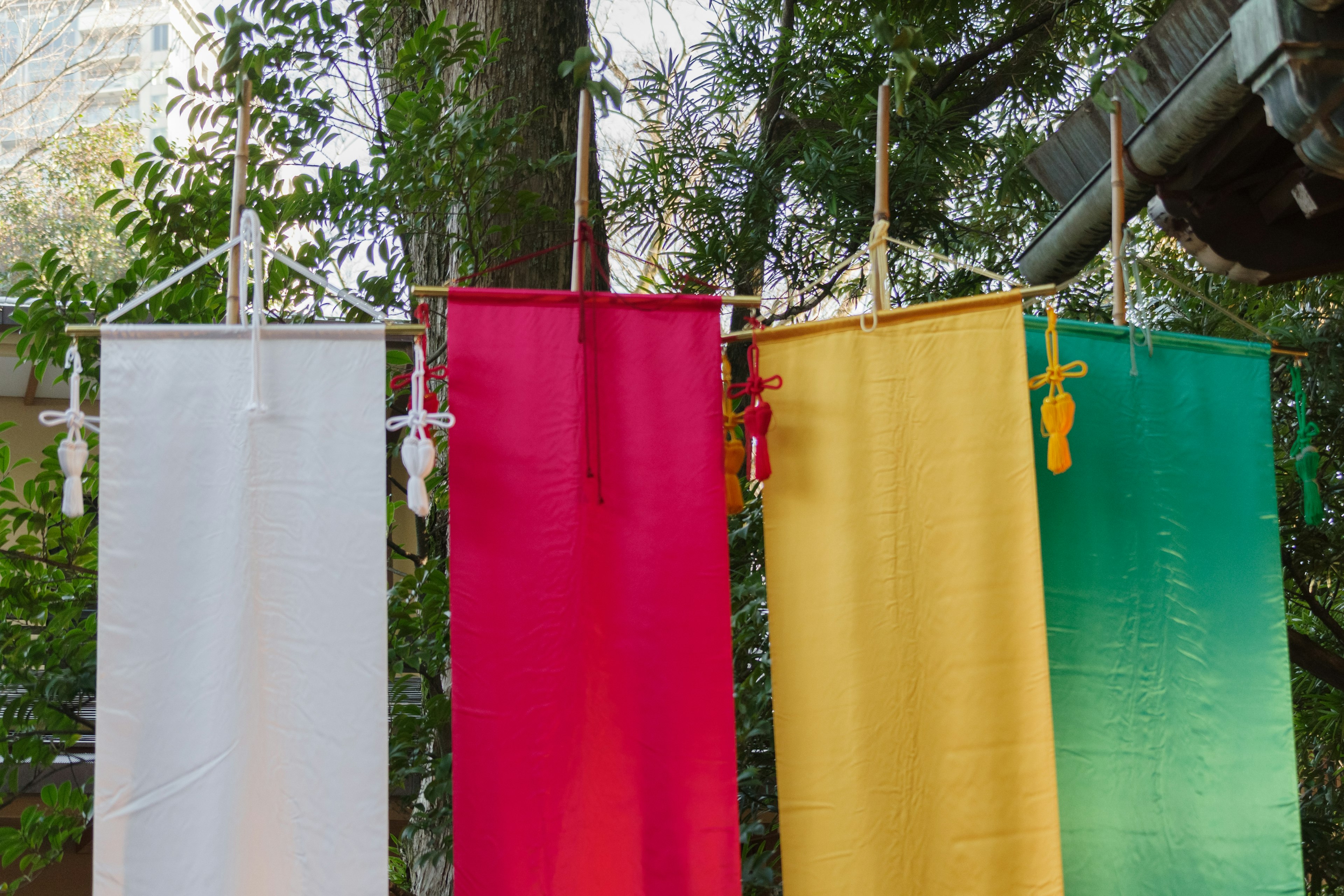 Four colorful fabric banners in white, red, yellow, and green hanging from branches