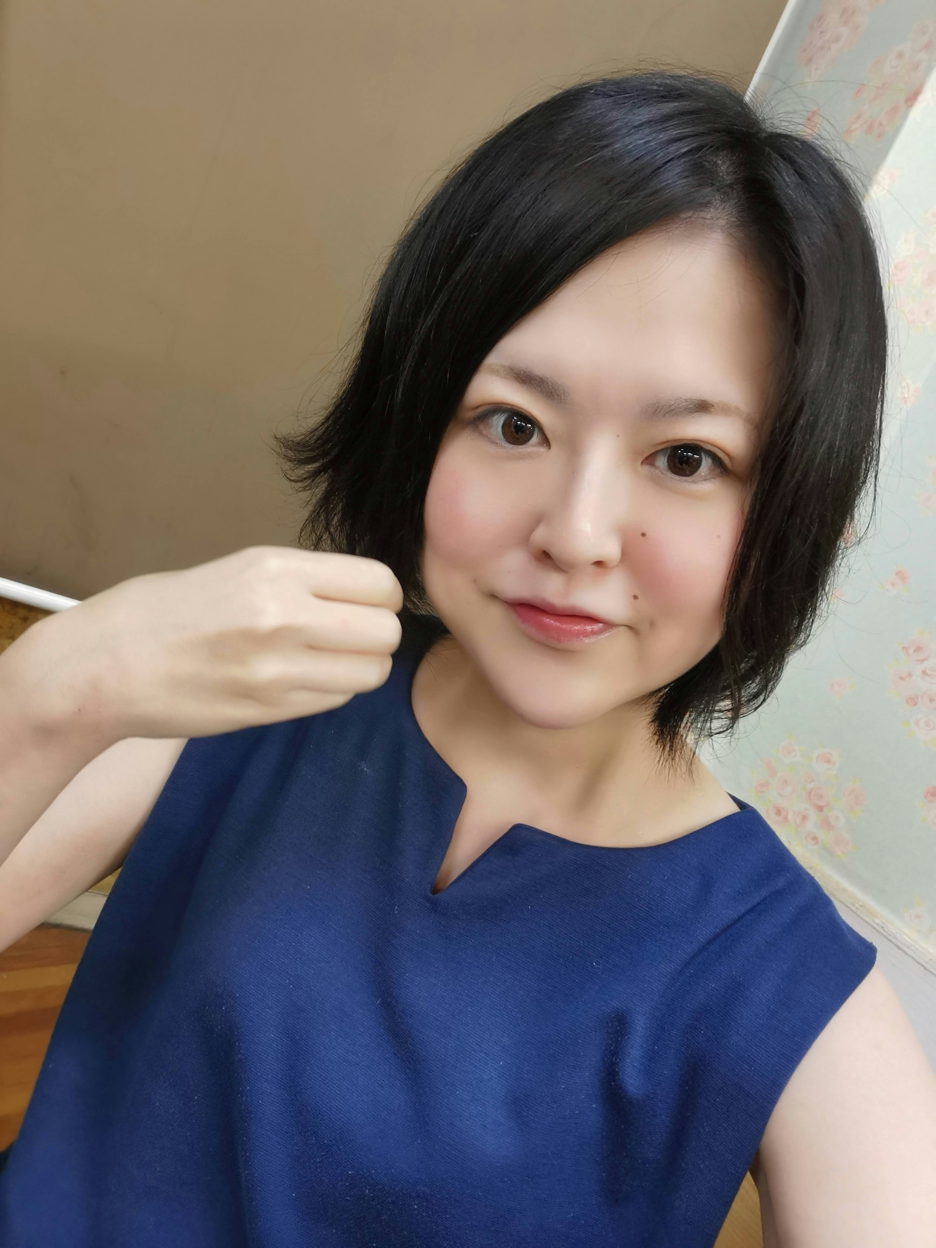 A woman wearing a blue top smiling and raising her hand