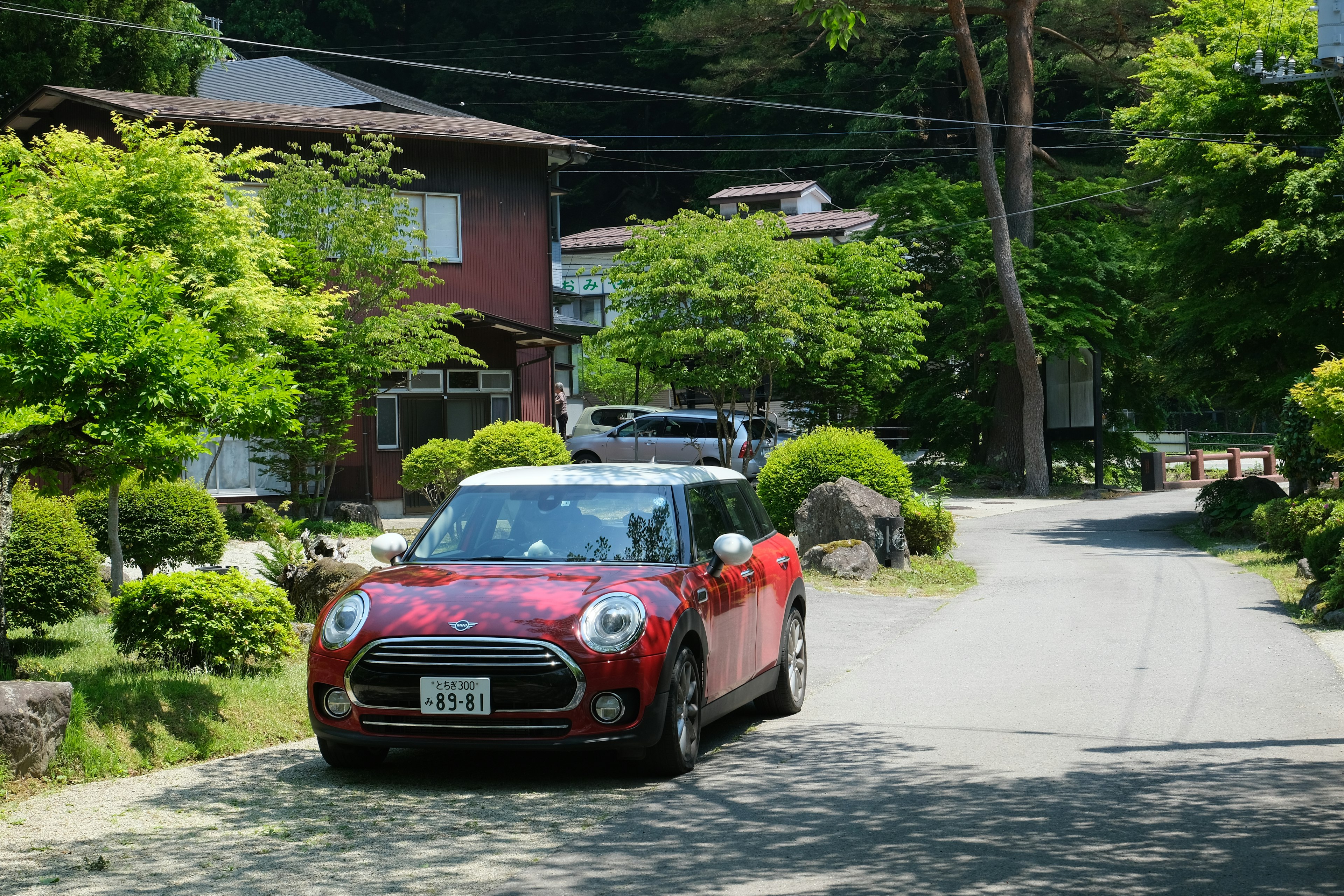 Sebuah Mini Cooper merah melaju di jalan perumahan yang tenang