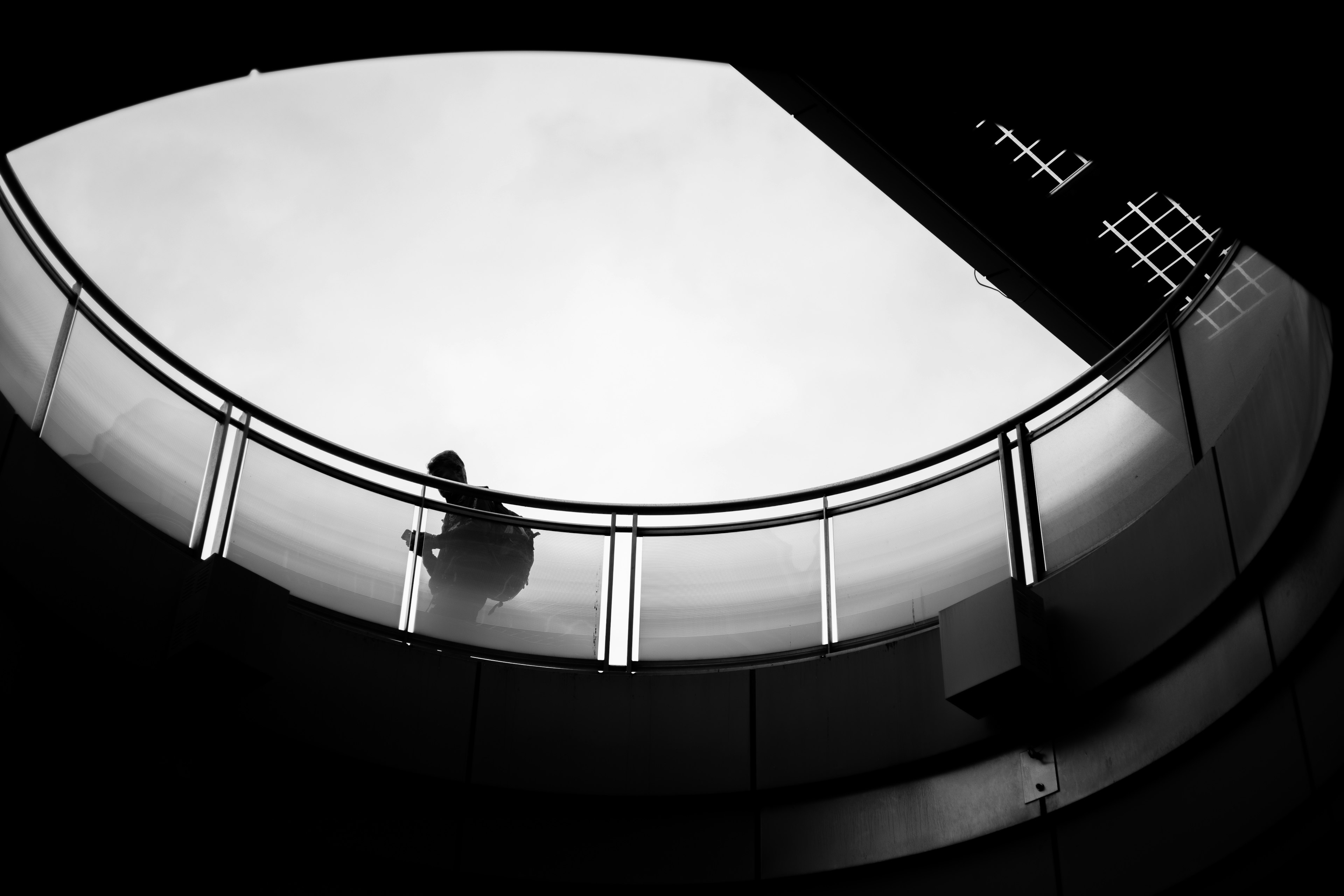 Silhouette of a person walking on a circular staircase against a cloudy sky