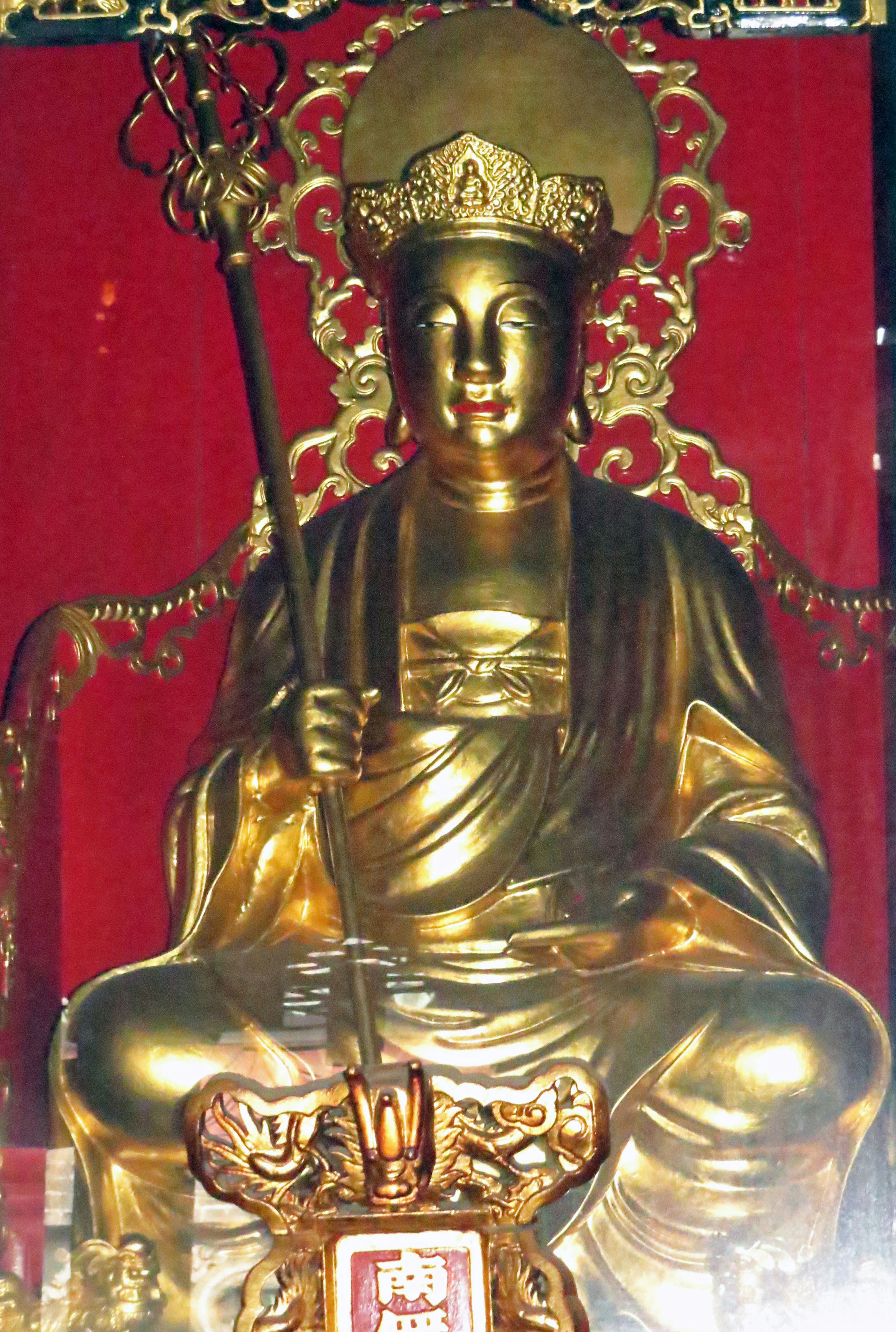 Golden statue of a deity seated on a throne with a red background