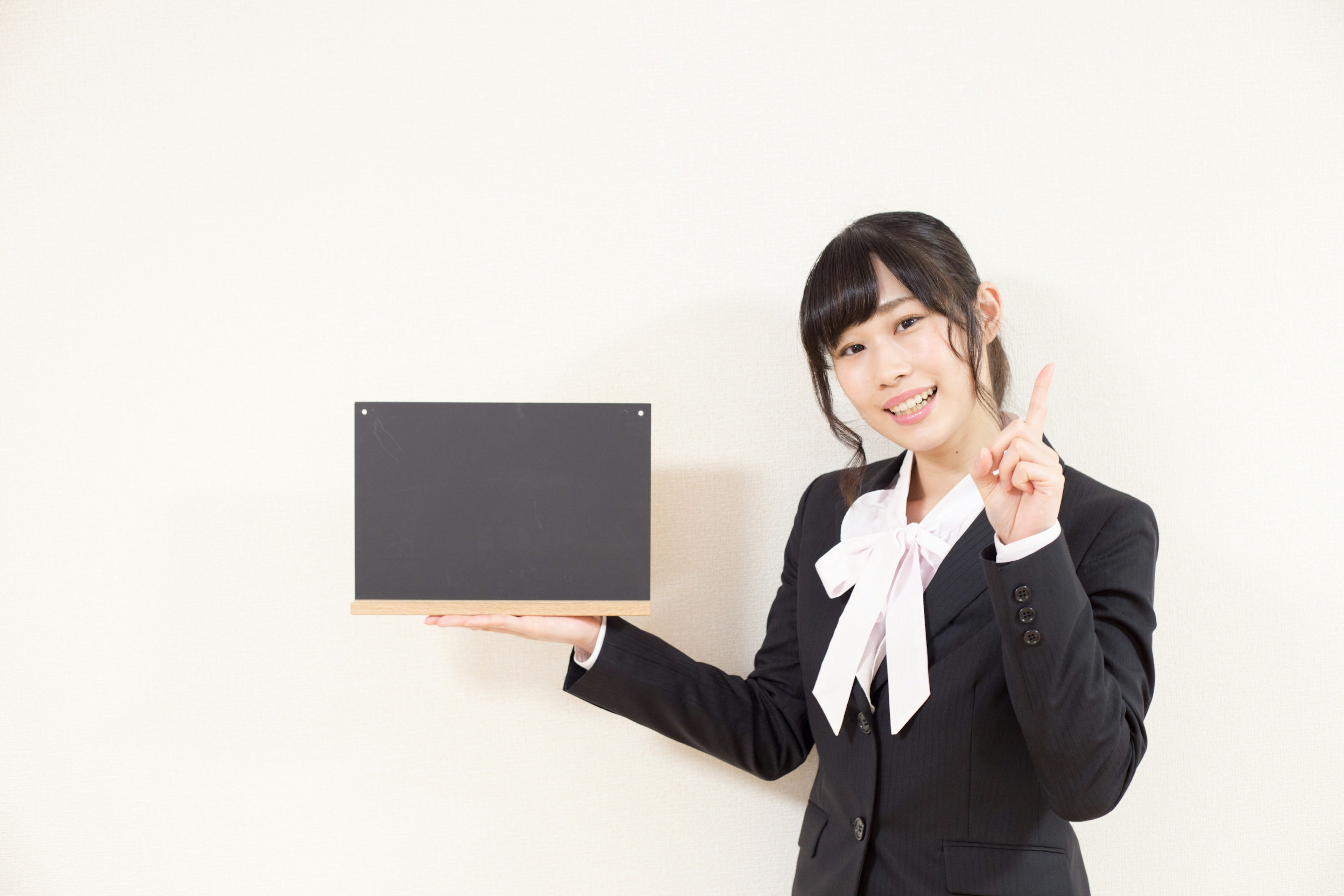 A woman in a business suit holding a black box and smiling with a raised finger