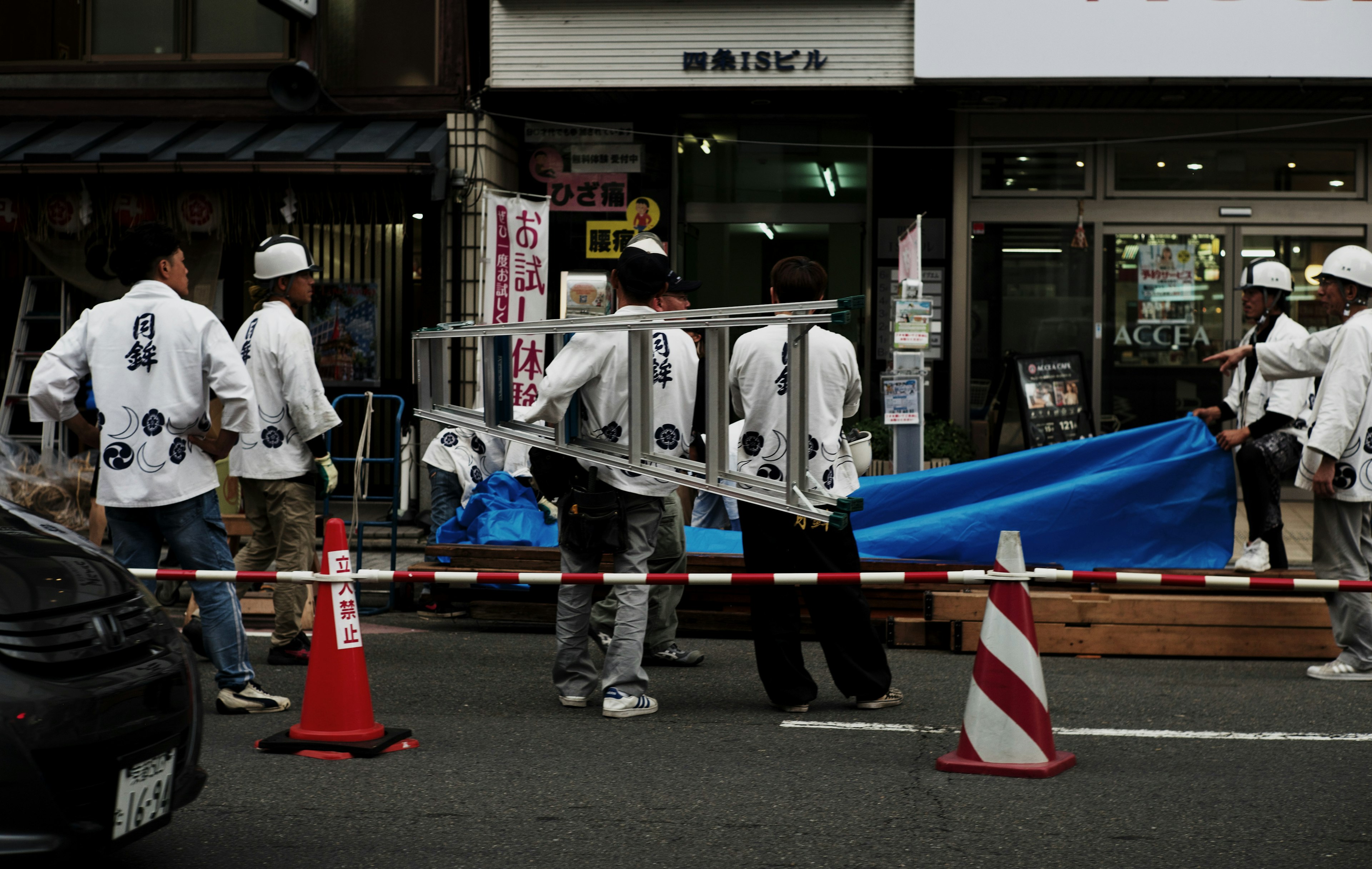 Workers carrying a blue tarp with traffic cones and barriers