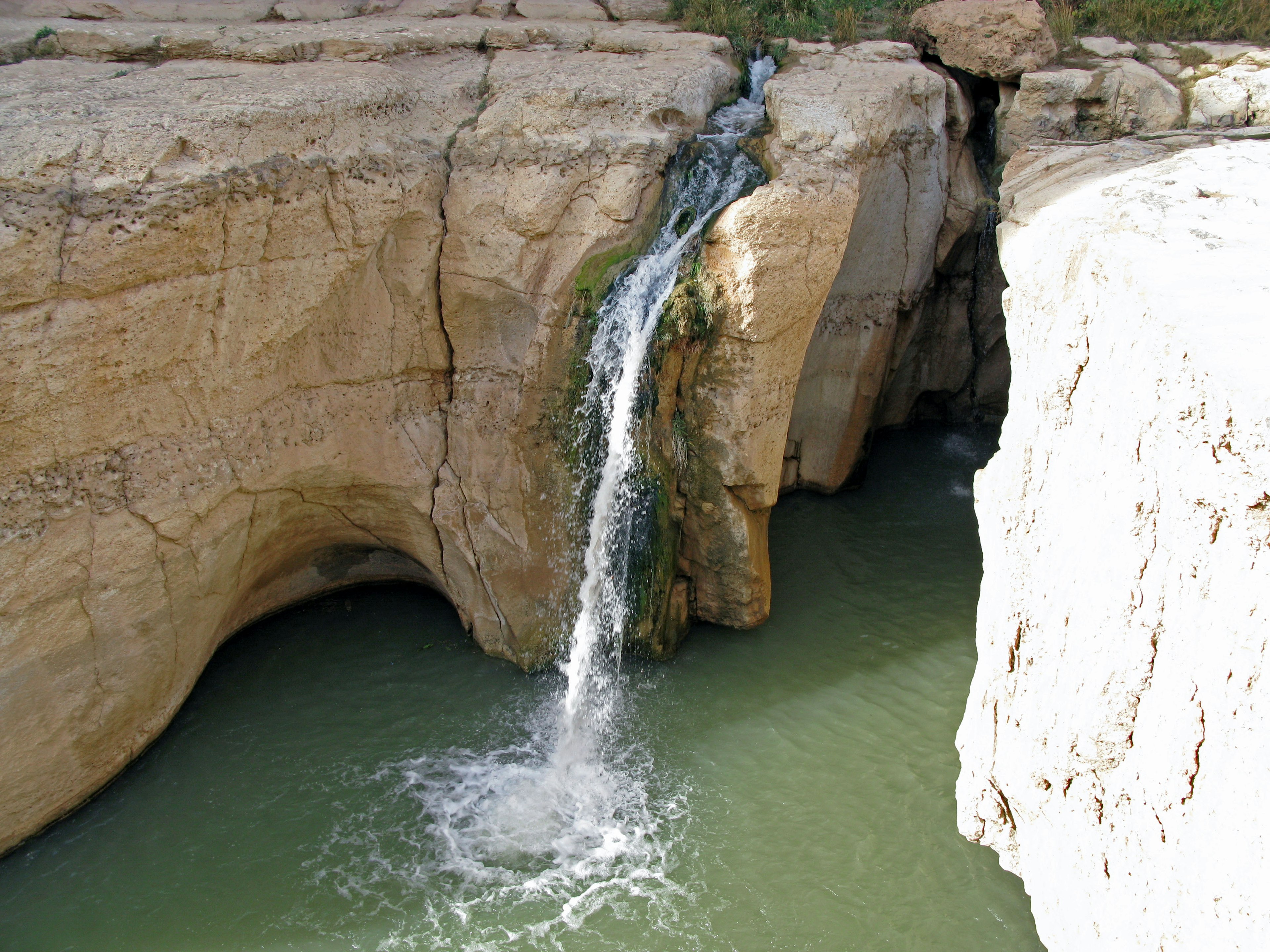 Wasserfall, der von einer Felsformation in einen grünen Pool fällt