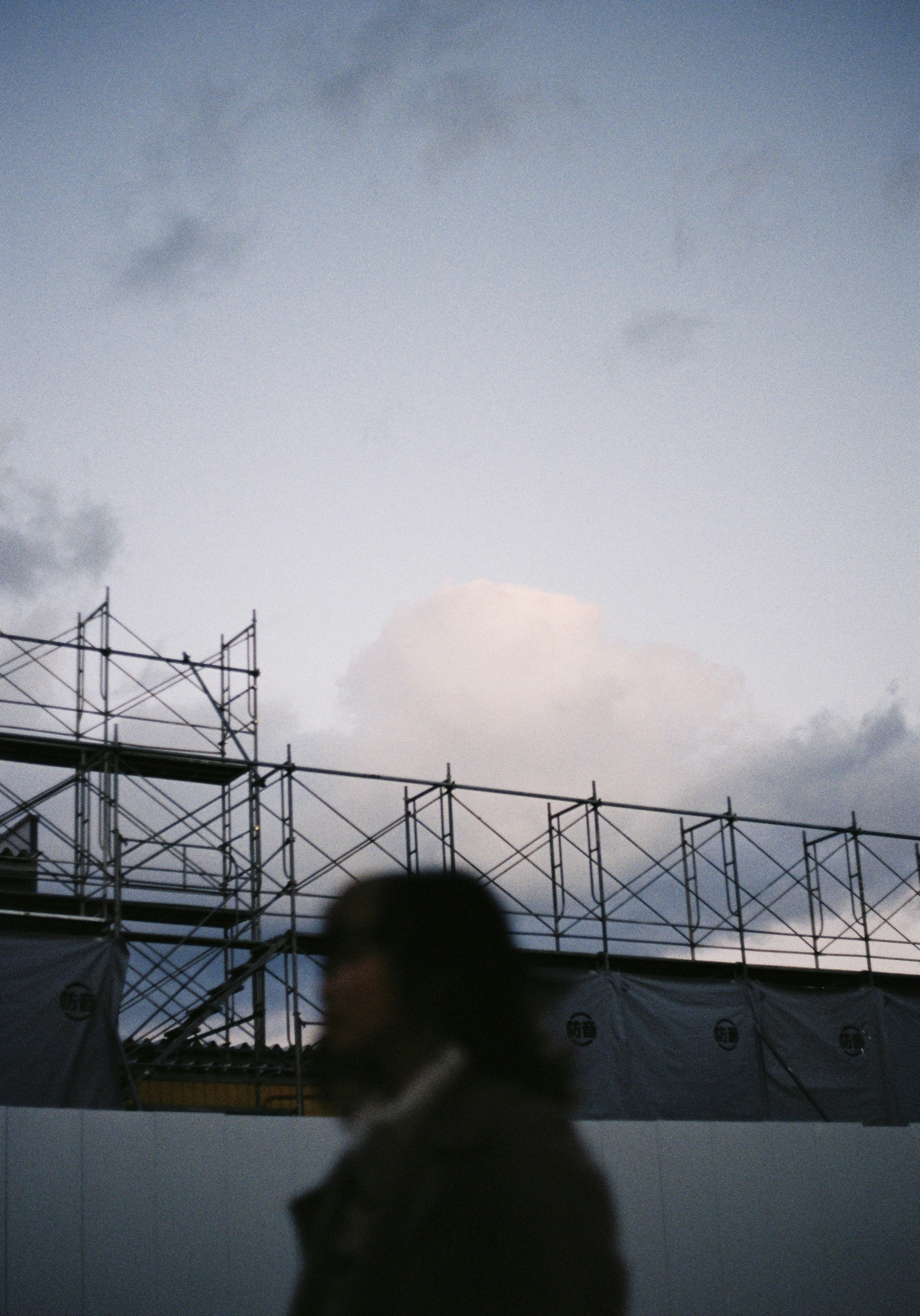 Silhouette de una persona caminando junto a un sitio de construcción con andamios y cielo nublado