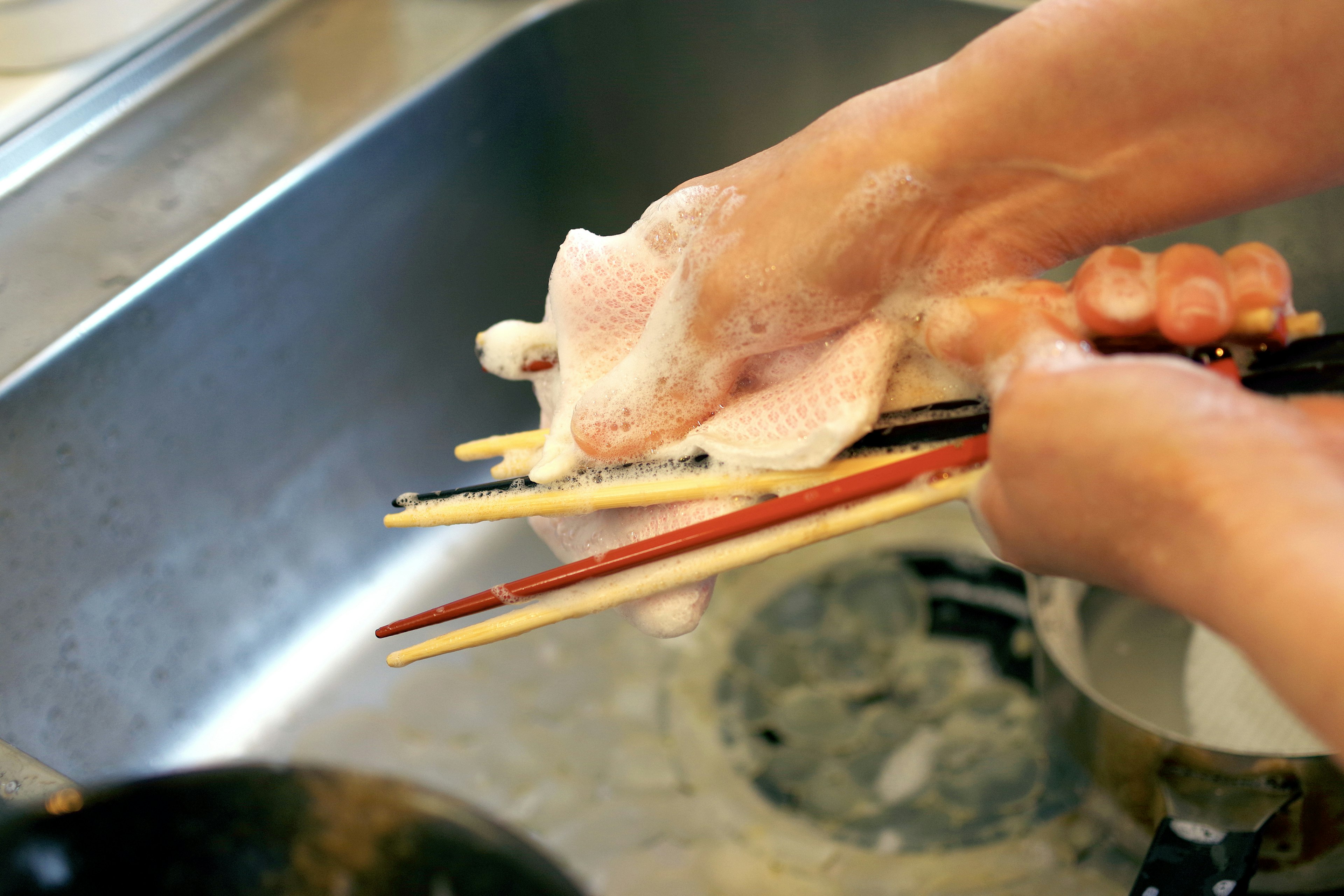 Image of hands washing chopsticks with soap and sponge