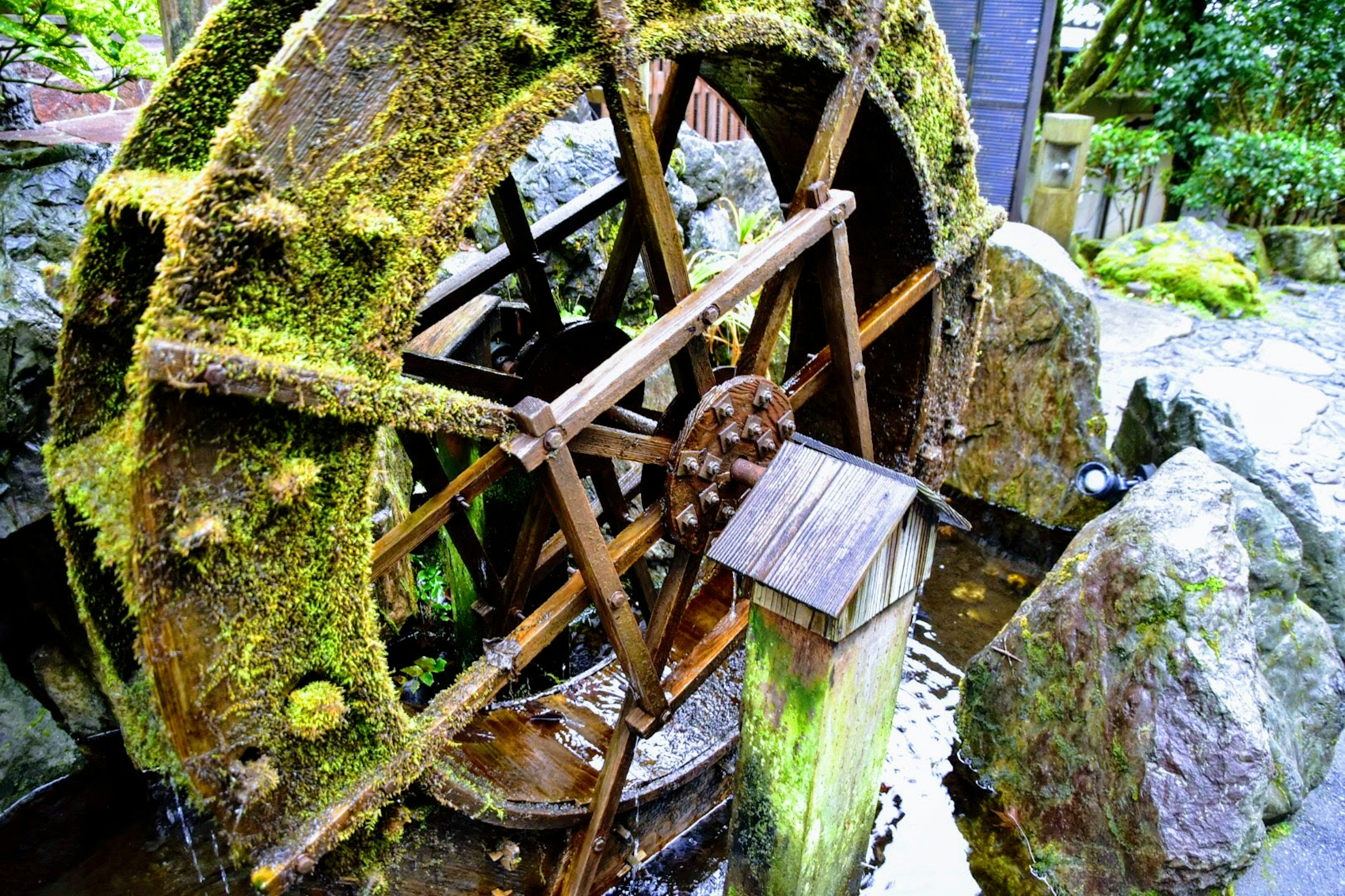 Moss-covered water wheel surrounded by stones