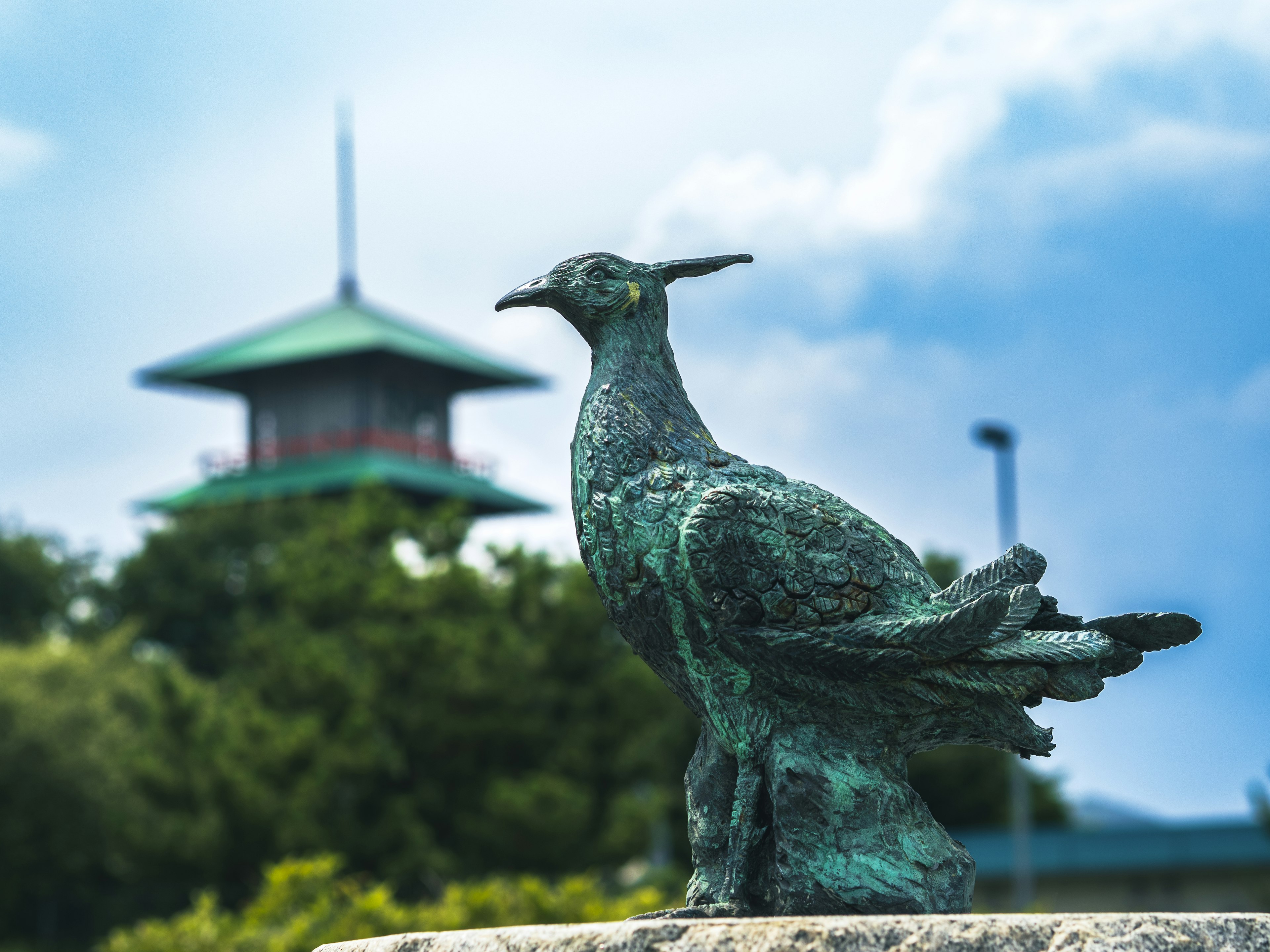 Scultura di uccello in bronzo verde con un edificio tradizionale sullo sfondo