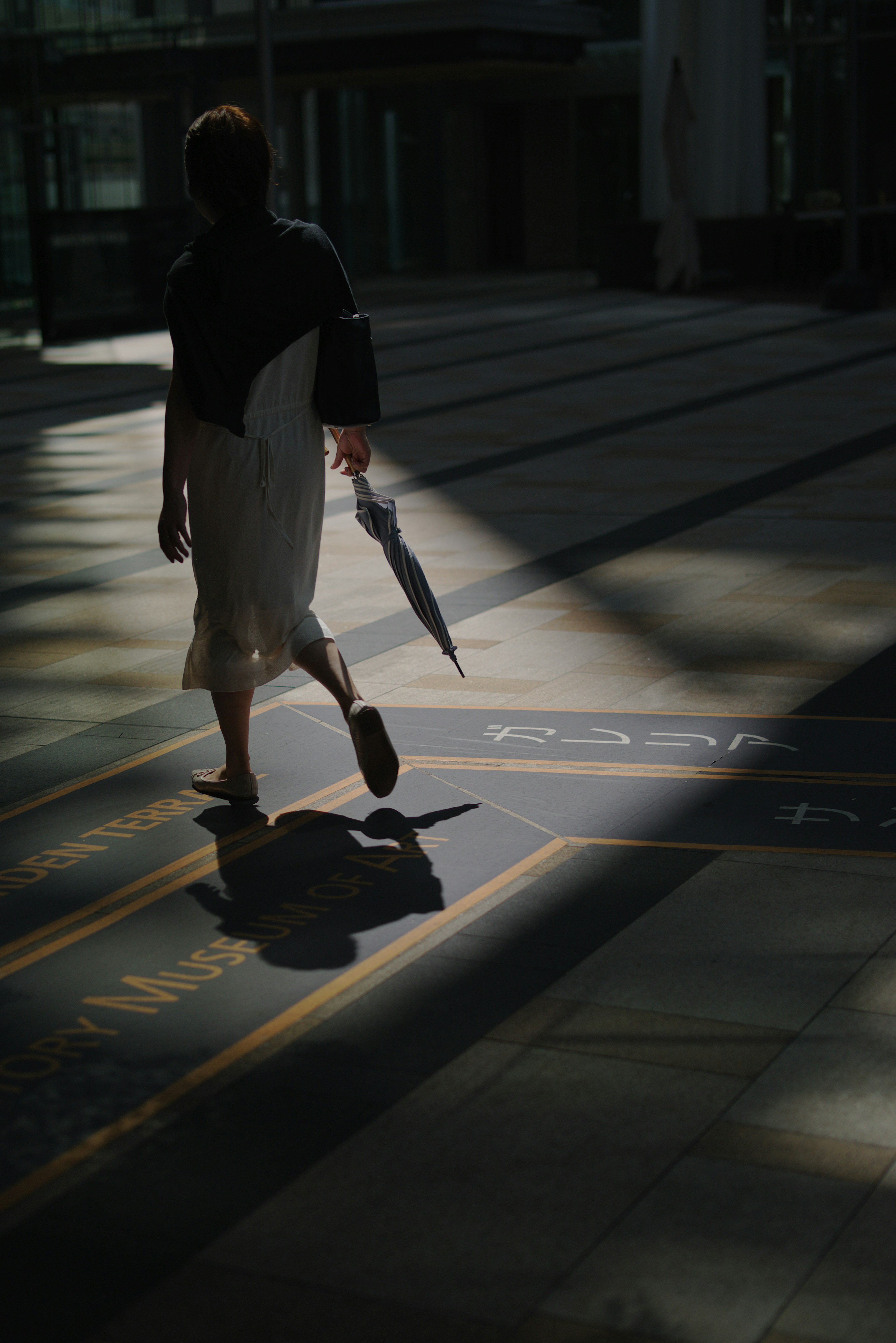 A person walking with an umbrella in a shadowed area