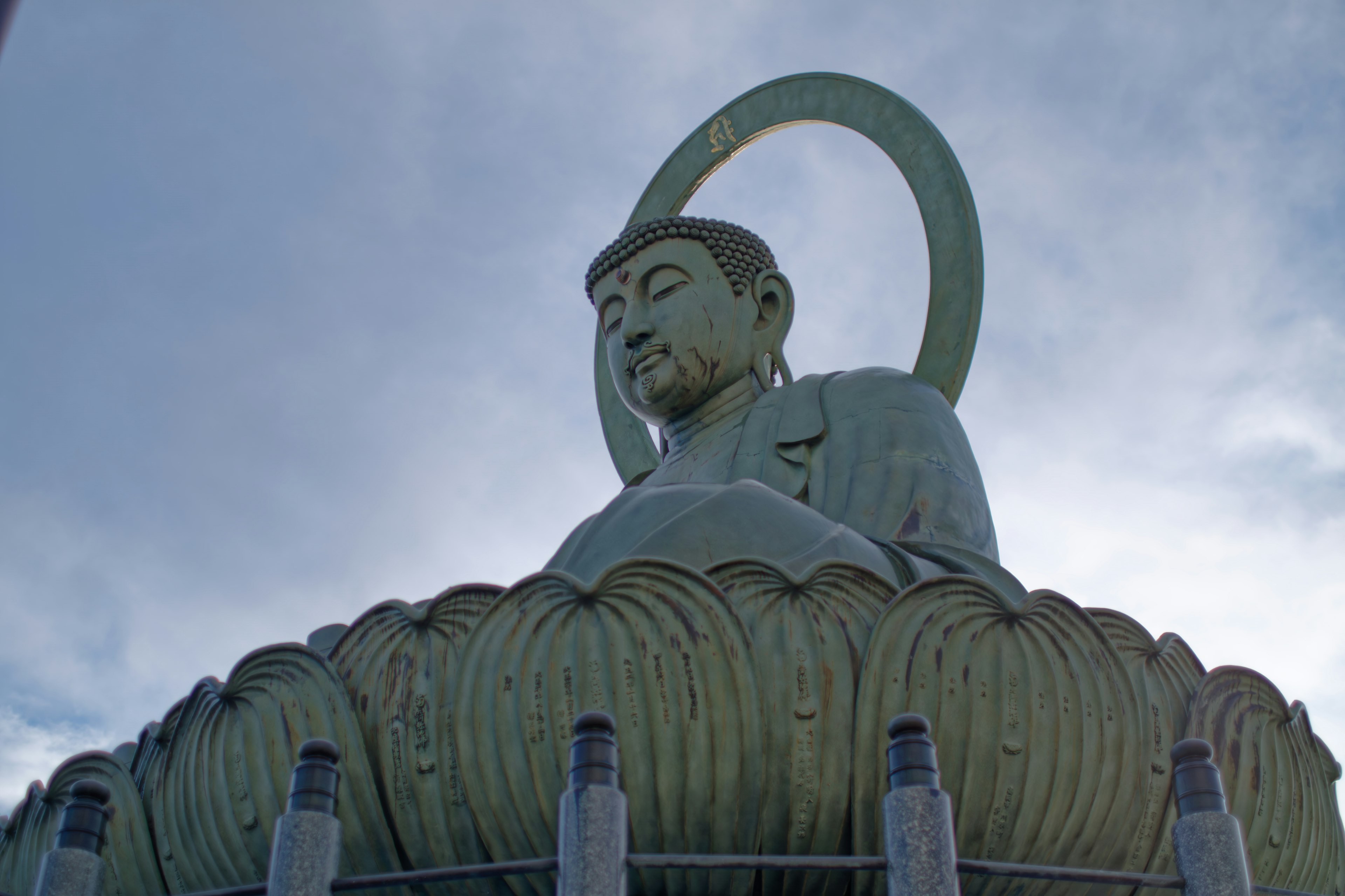 Large Buddha statue seated on a lotus pedestal against a cloudy sky