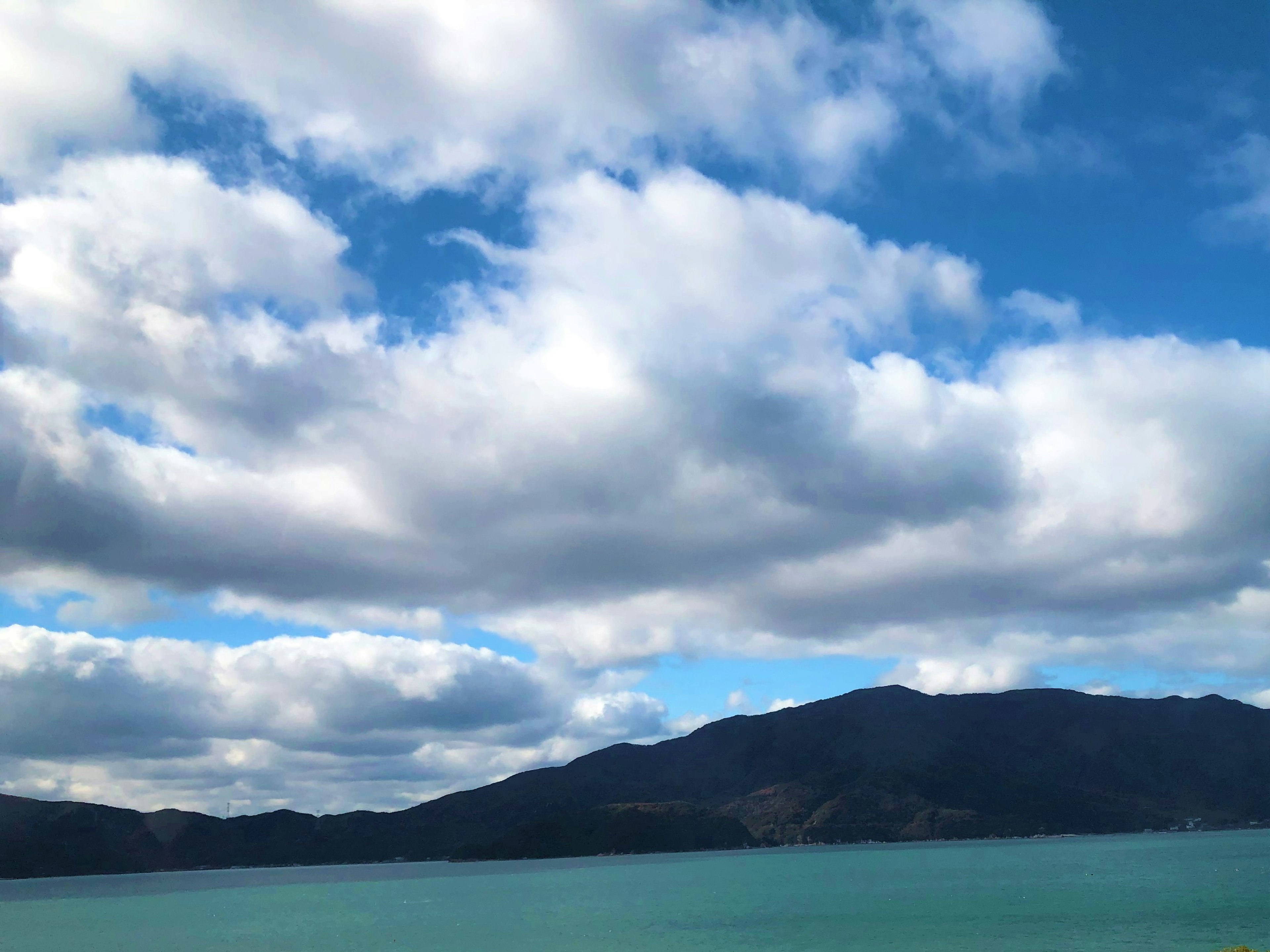 Pemandangan dengan langit biru dan awan putih menampilkan danau dan pegunungan