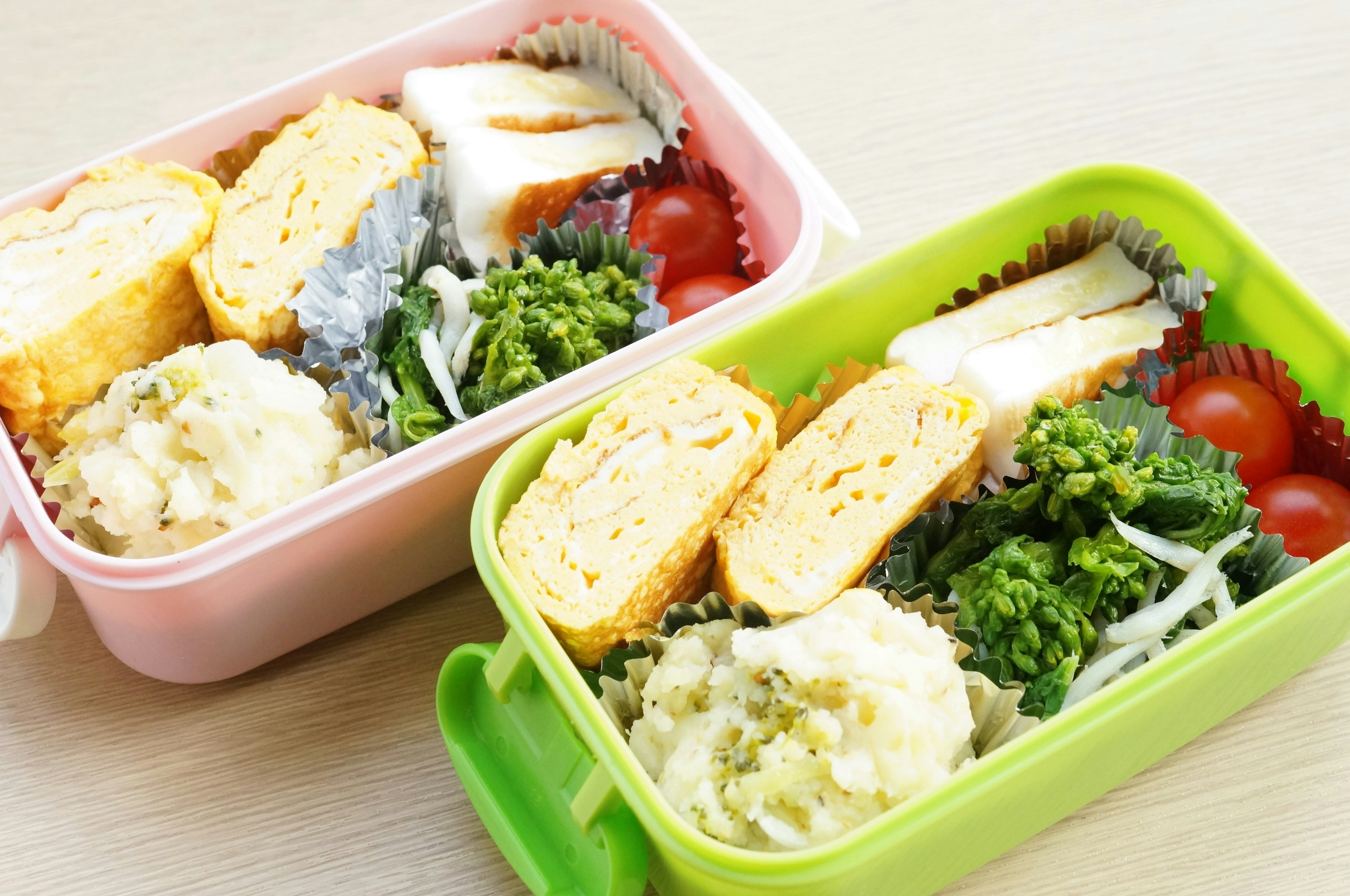 Two colorful bento boxes filled with various Japanese dishes