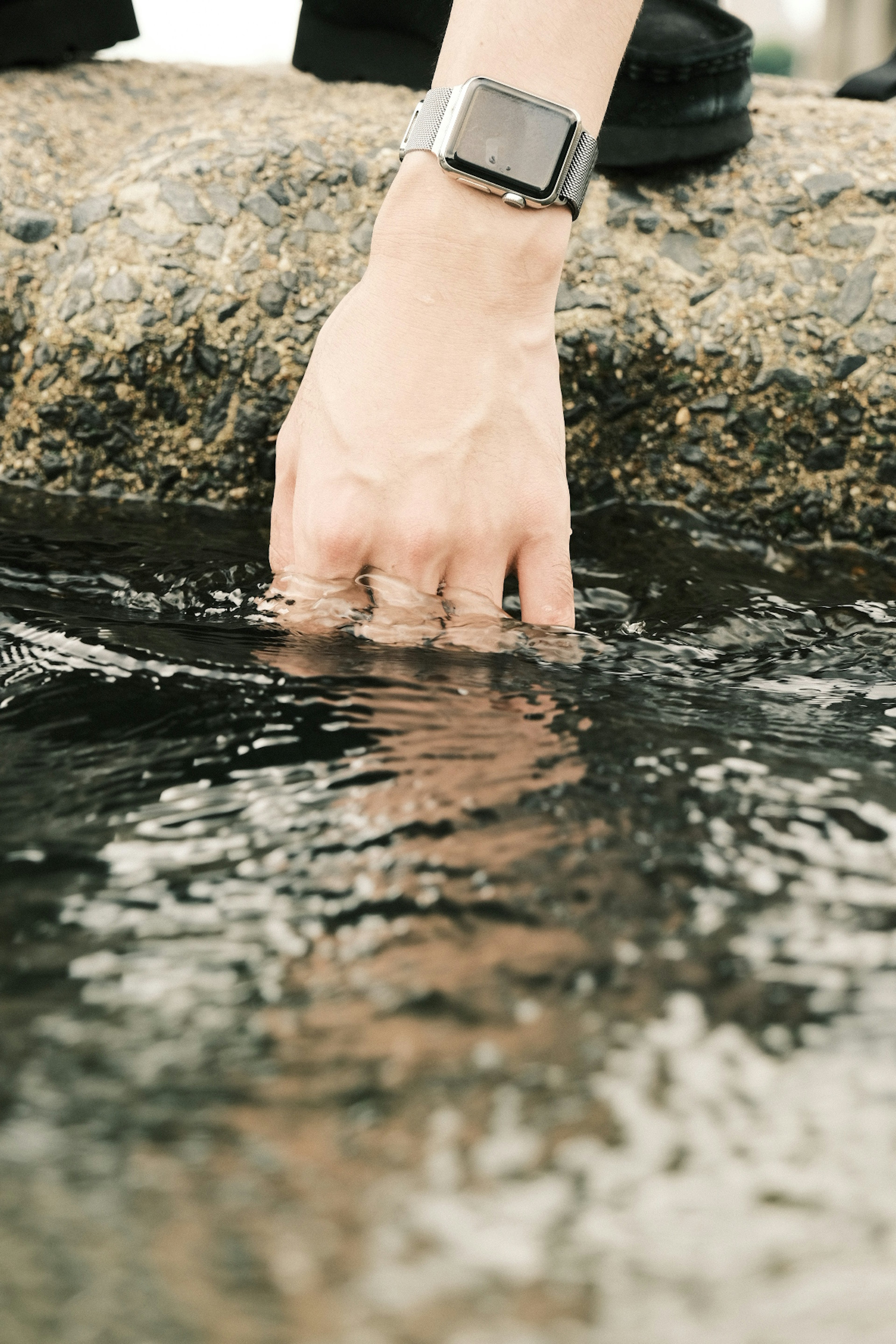 水面に手を浸す人物の手と石の縁