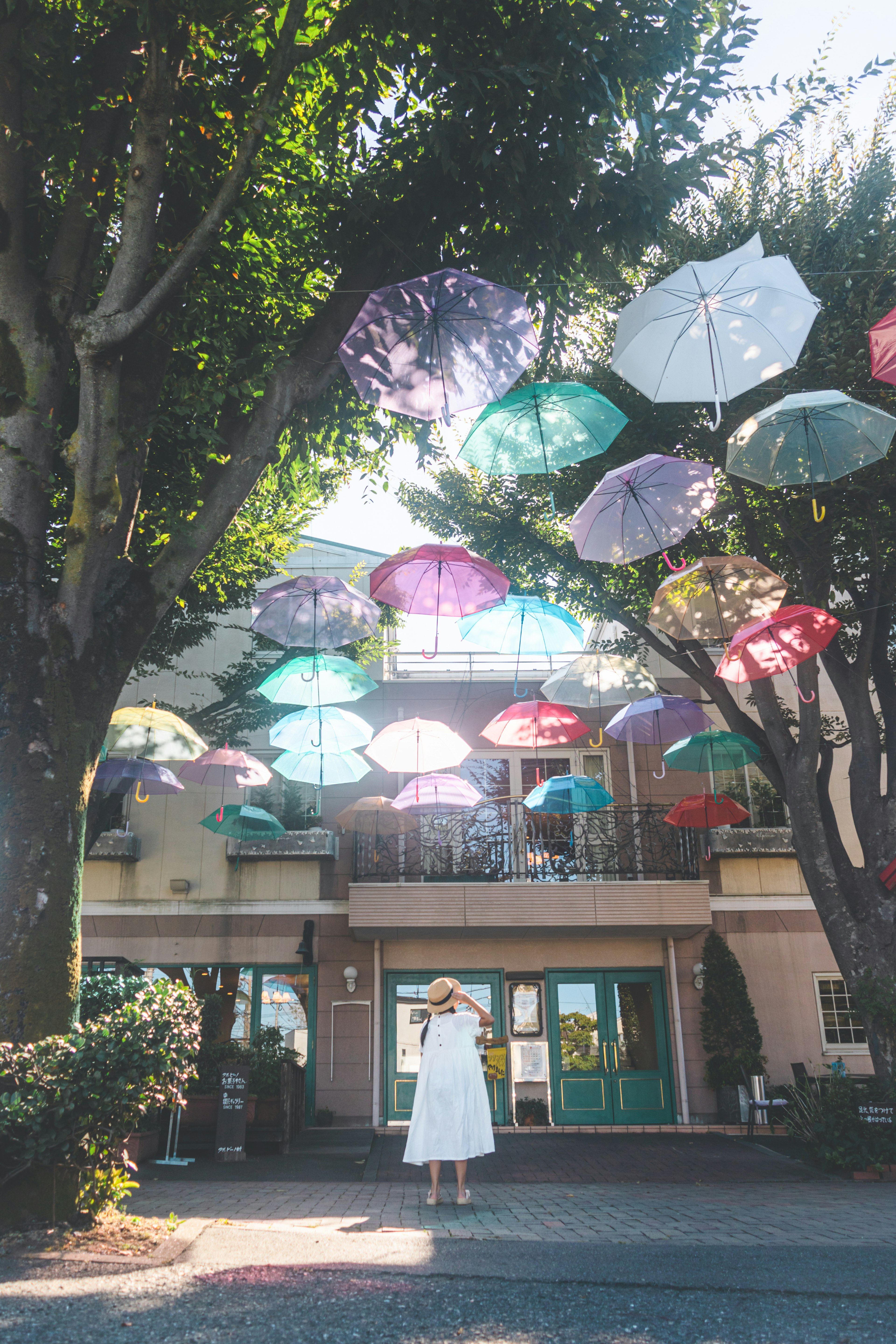 A woman in a white dress standing under colorful umbrellas hanging from trees