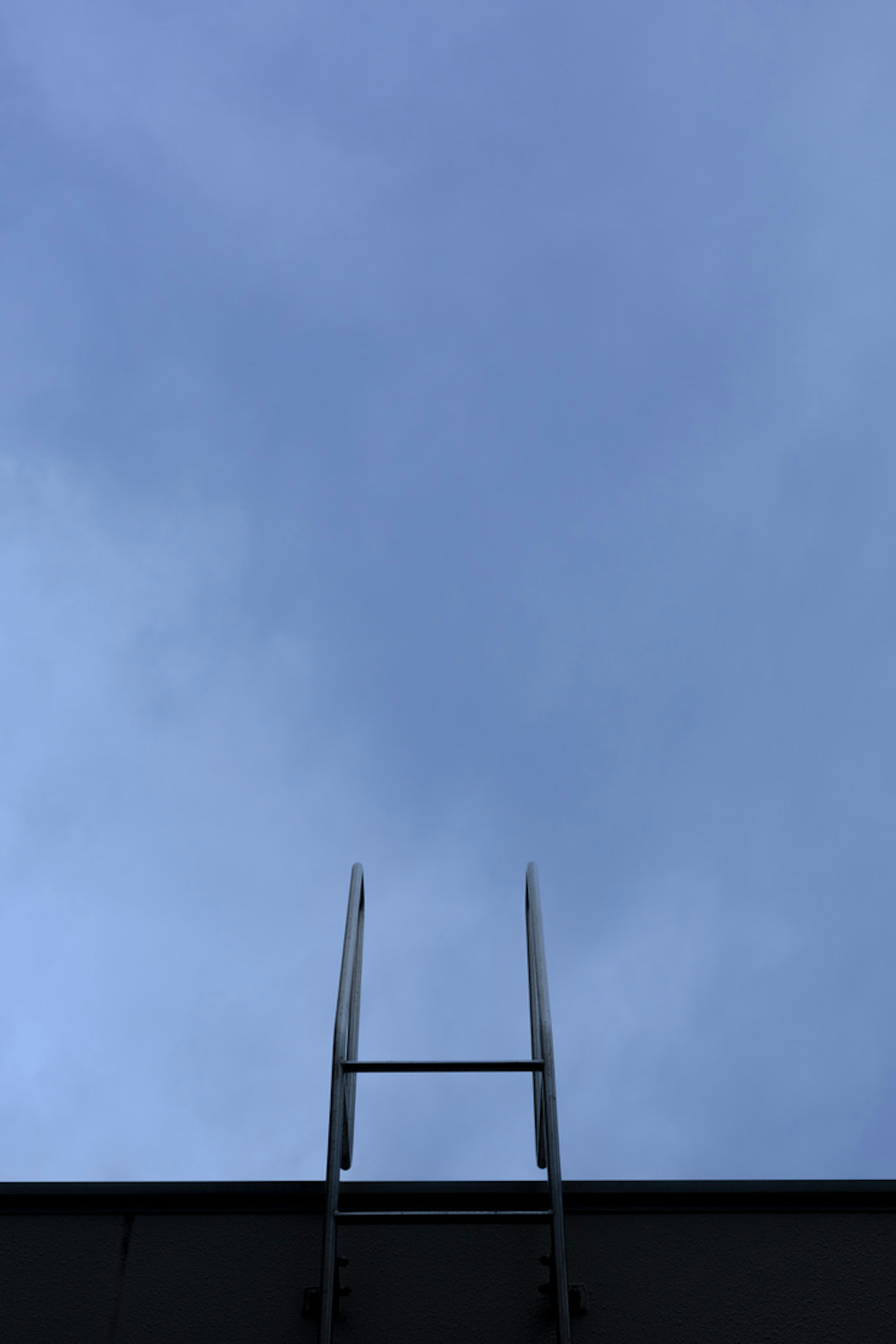 Una escalera de metal que llega a un cielo azul nublado