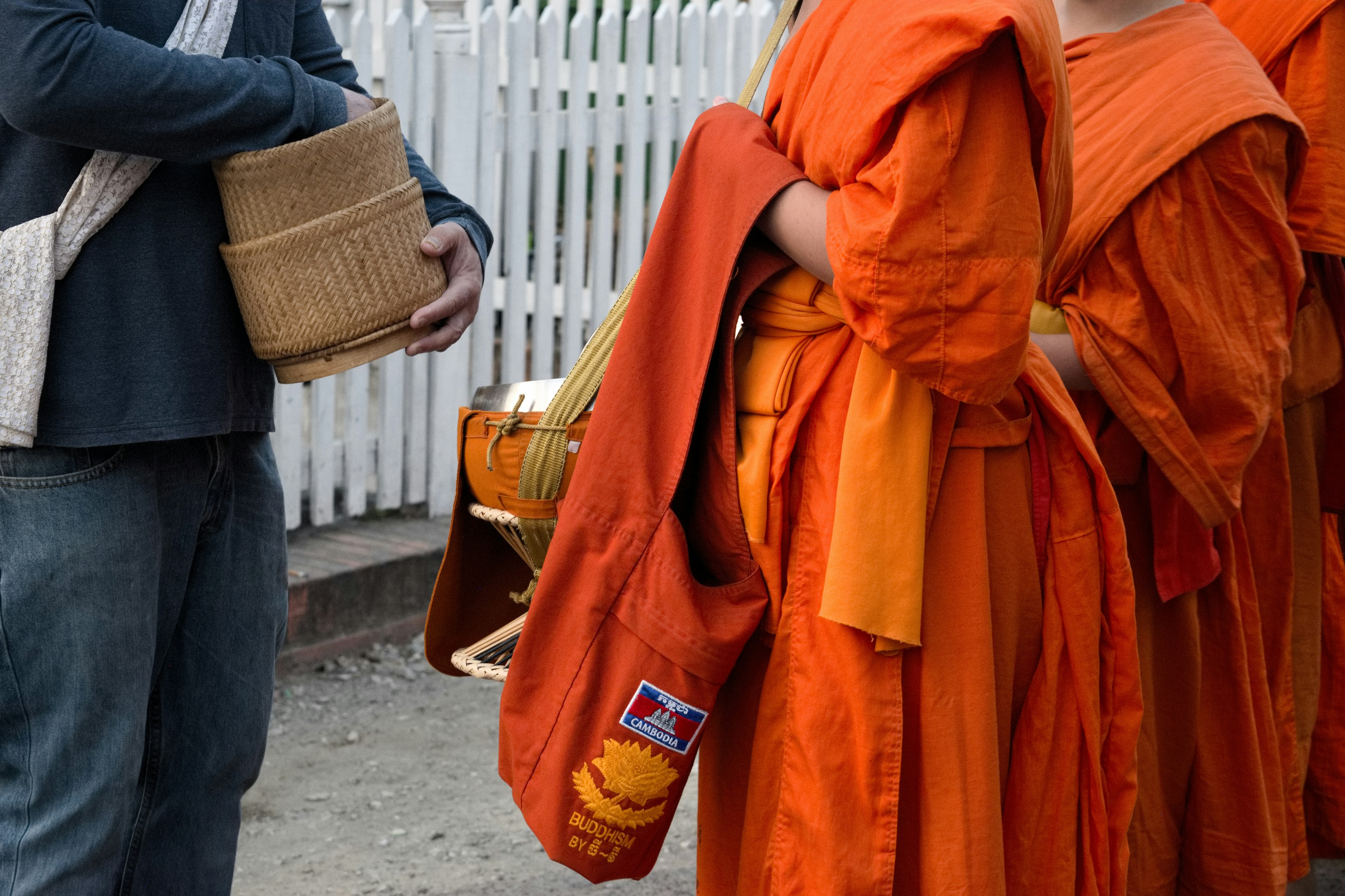 Scene of orange-robed monks with a person holding a basket in the foreground