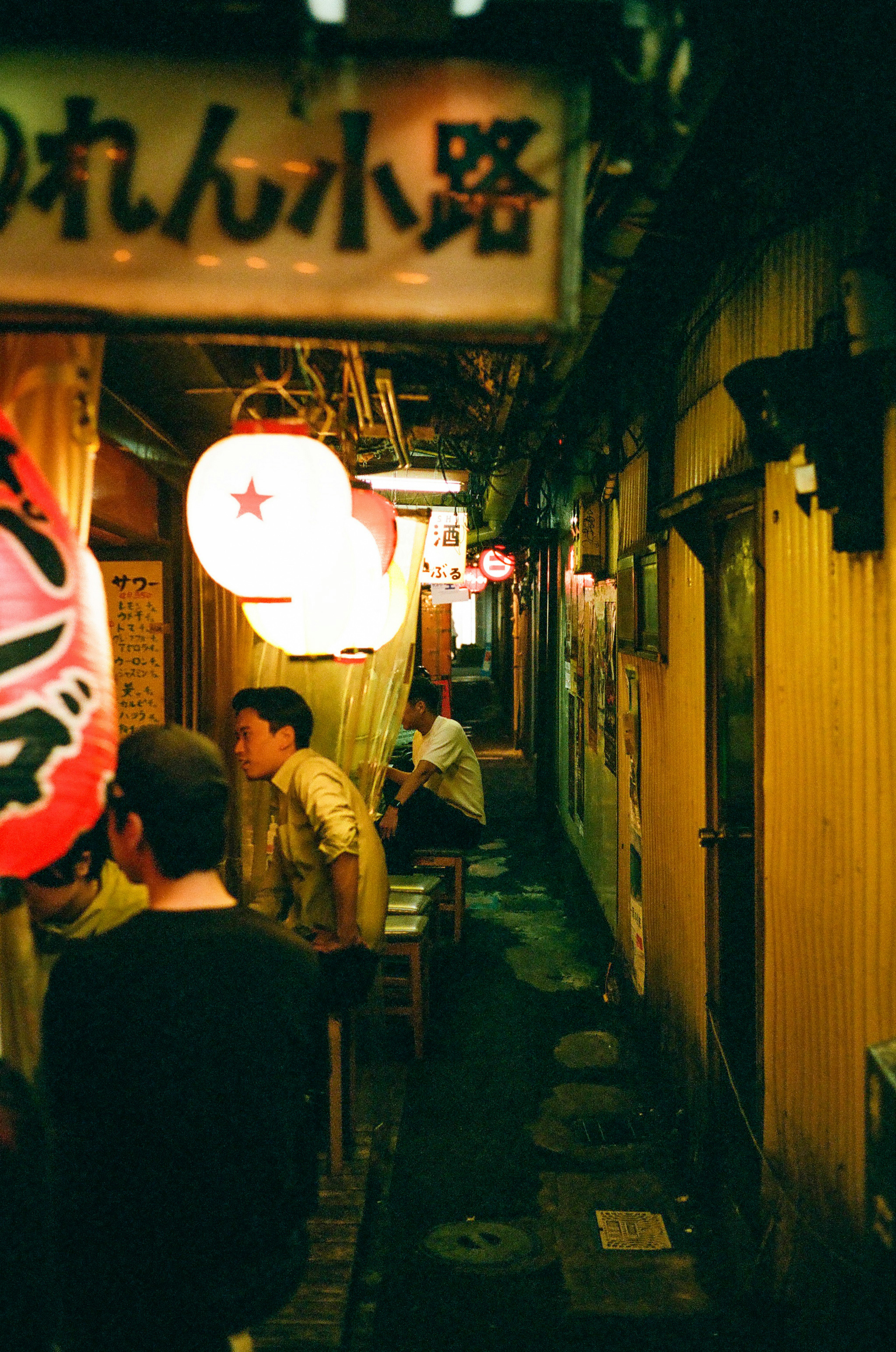 Allée étroite bordée de panneaux de restaurant et de lanternes la nuit