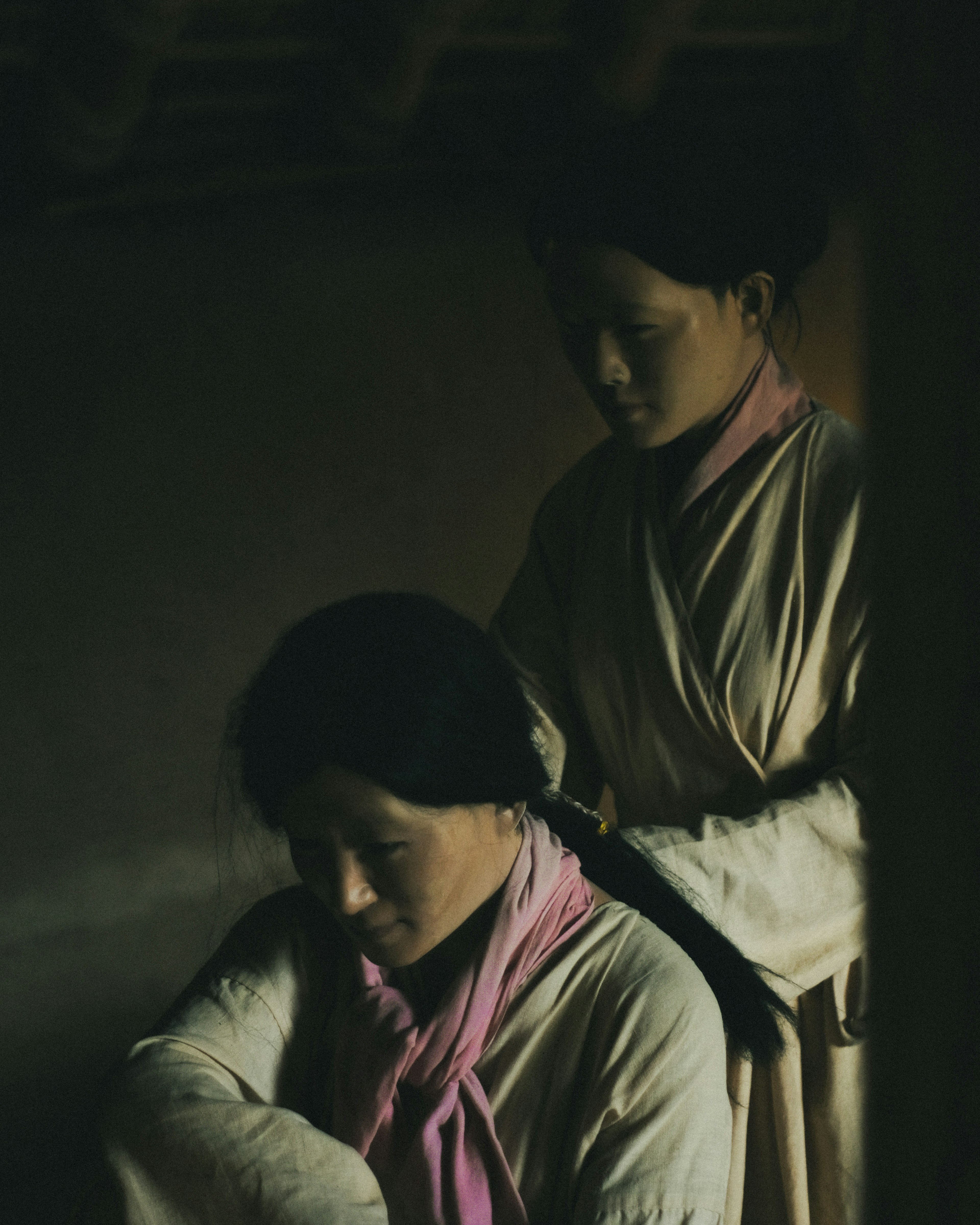 Dos mujeres con vestimenta tradicional una está atando el cabello de la otra