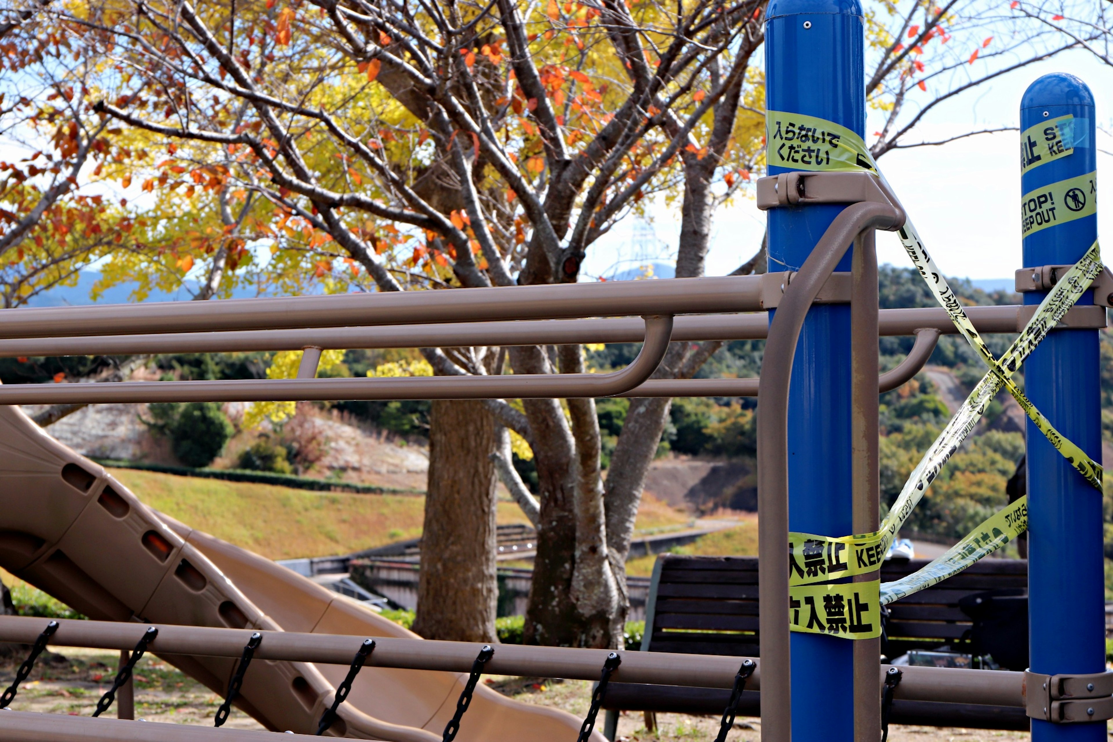 Rutsche auf dem Spielplatz mit blauen Pfosten, die in gelbem Warnband in einer herbstlichen Umgebung eingewickelt sind