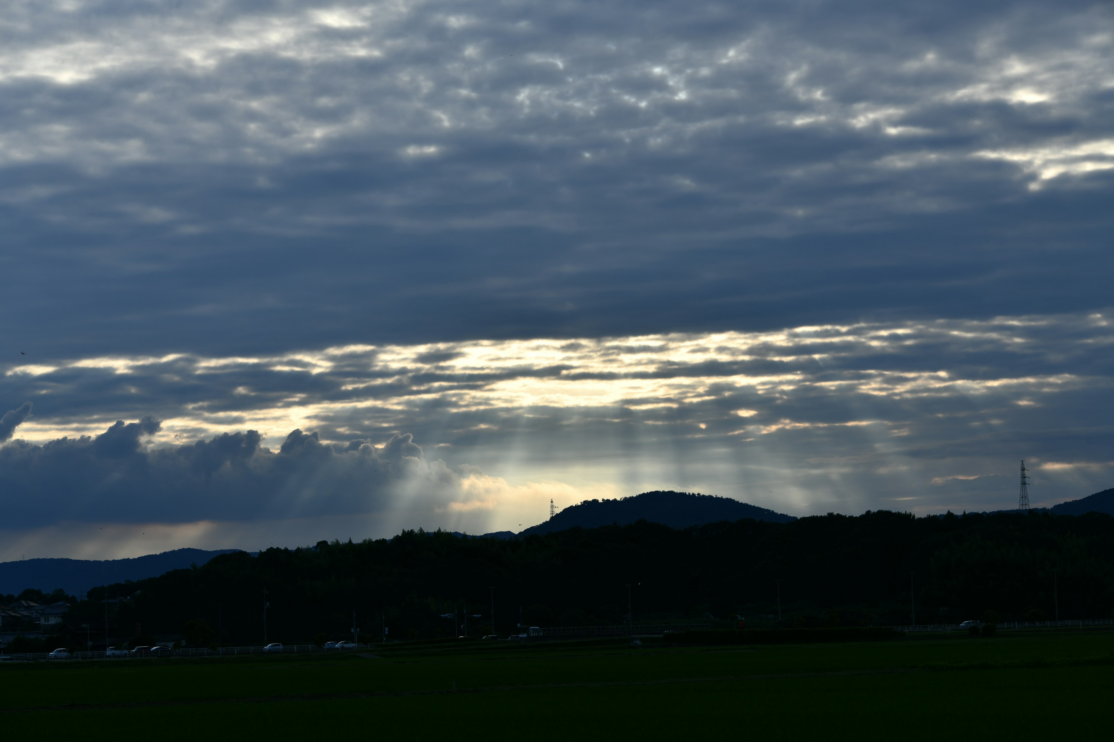 Landschaft mit bewölktem Himmel und Lichtstrahlen, die Hügel und grüne Felder beleuchten