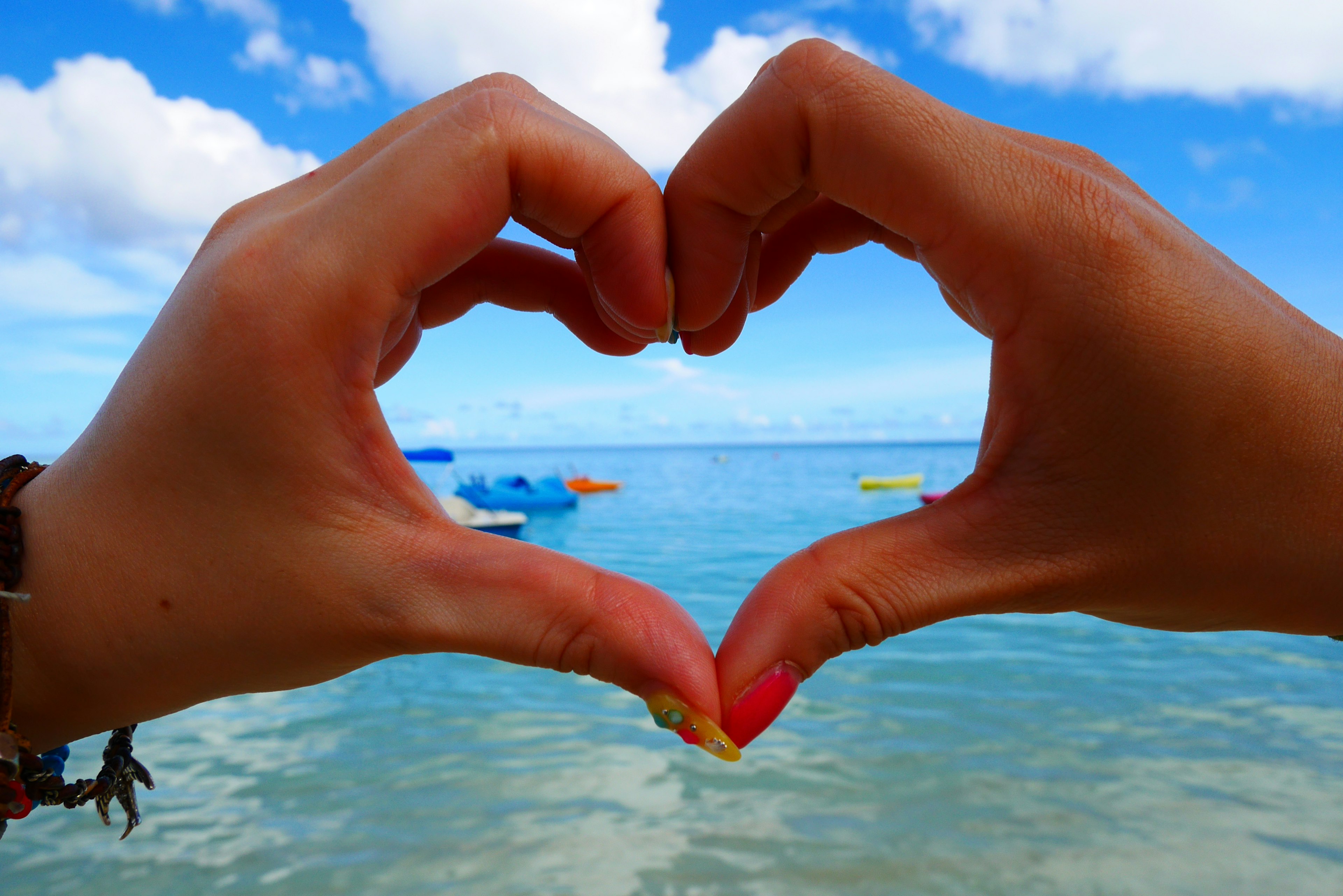 Mani che formano un cuore contro un cielo e un oceano blu