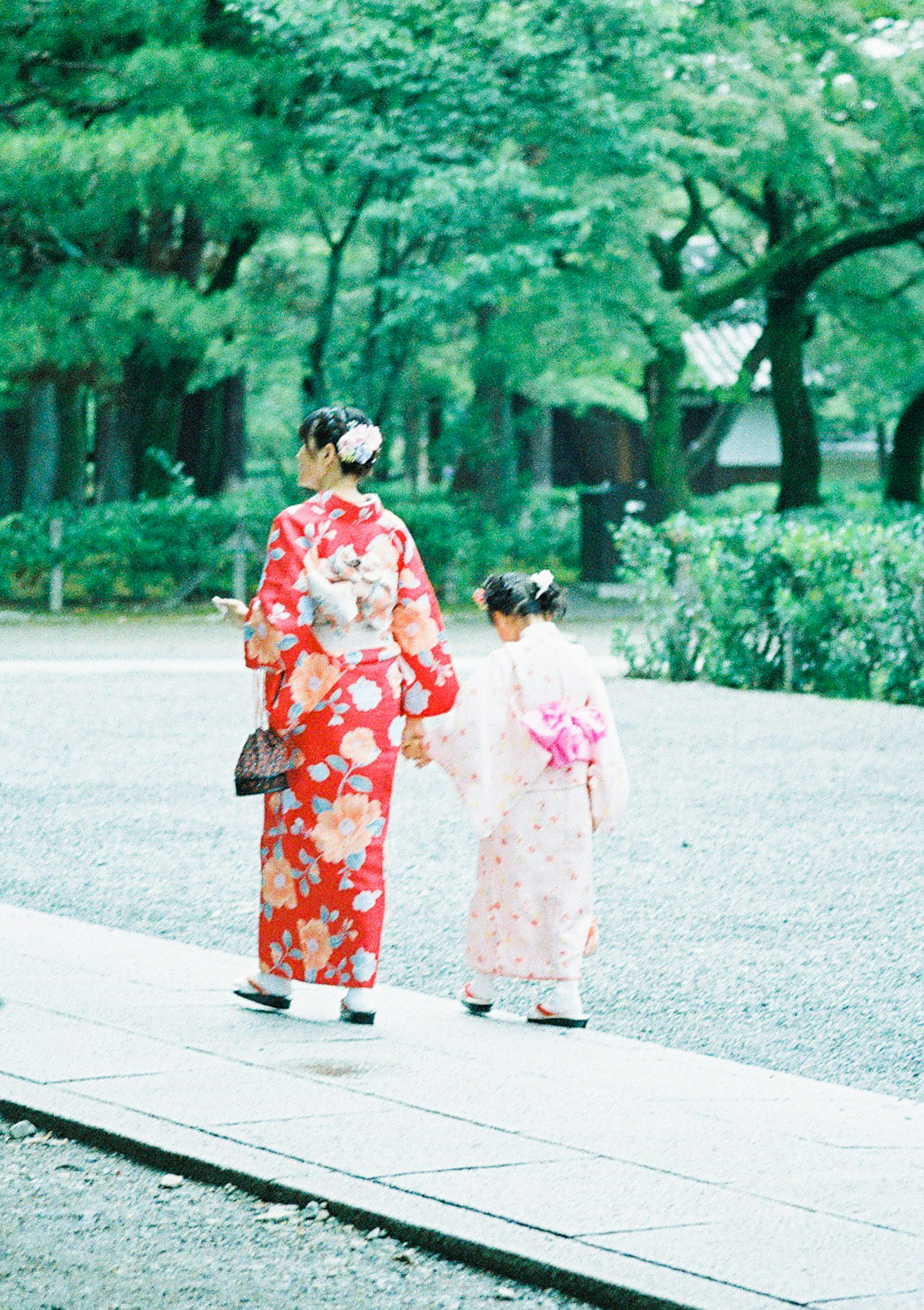 Une mère en kimono floral rouge et sa fille en kimono rose marchant main dans la main