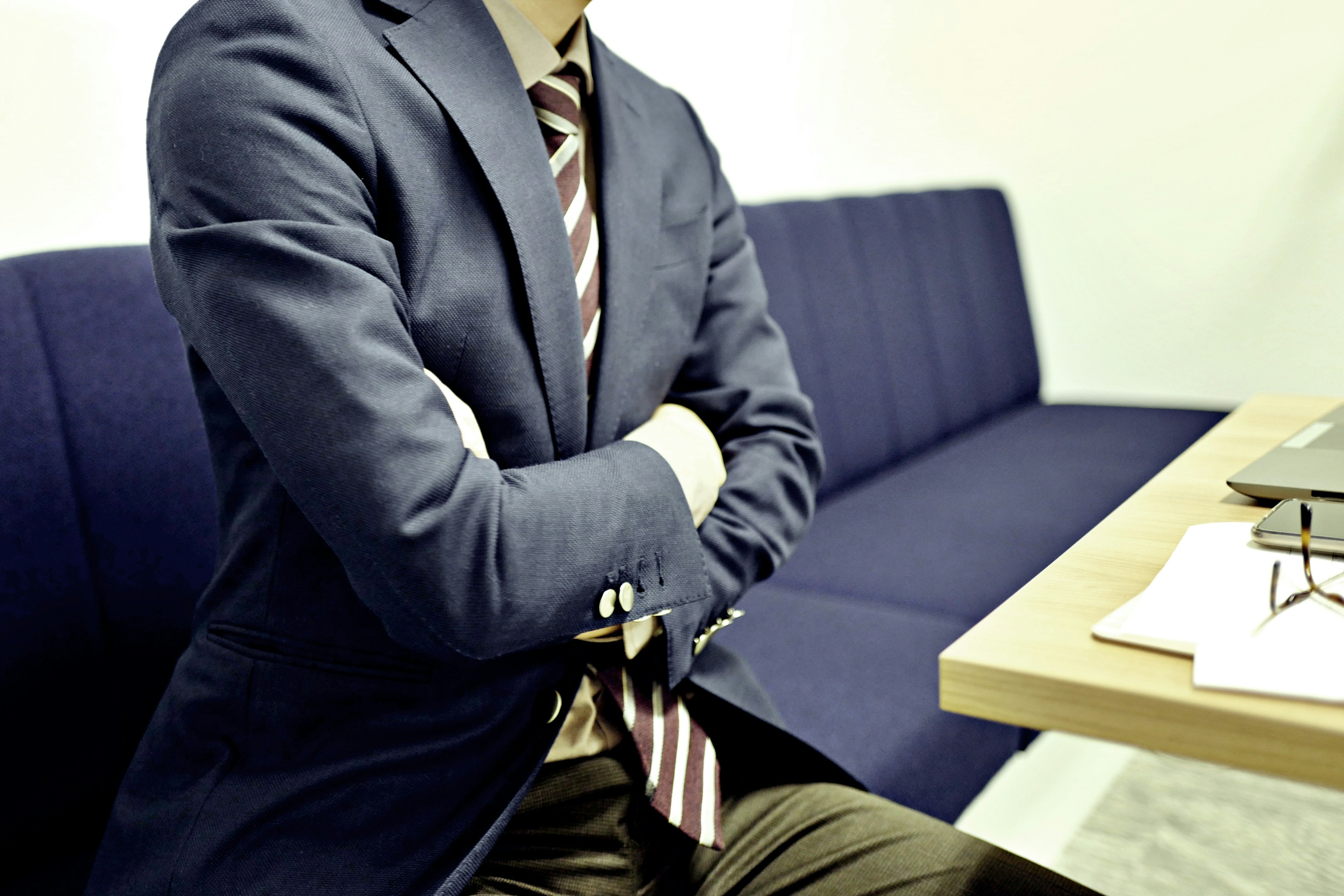 A man in a suit with crossed arms sitting beside a blue couch