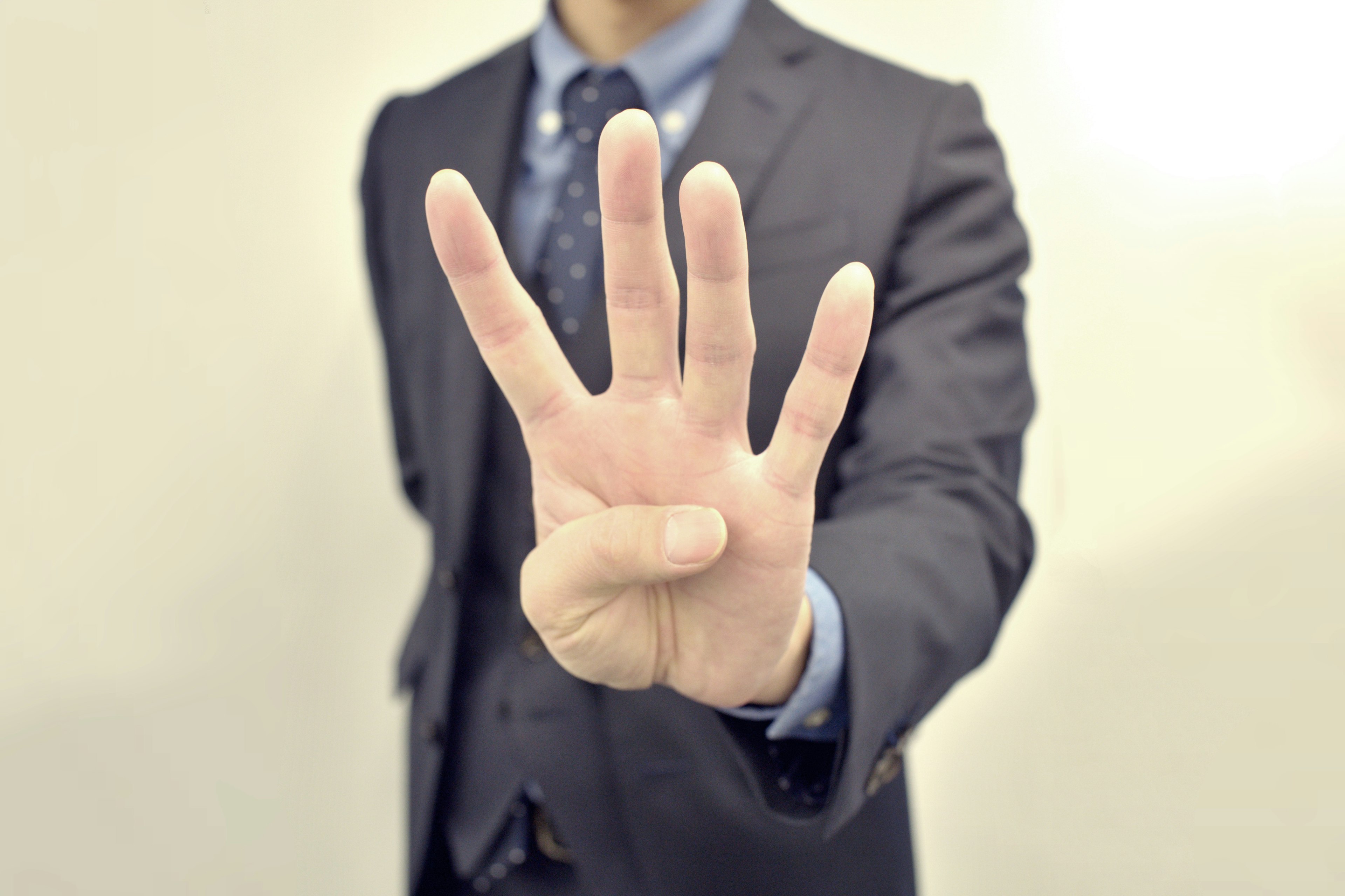 A man in a suit holds up four fingers with his hand extended forward