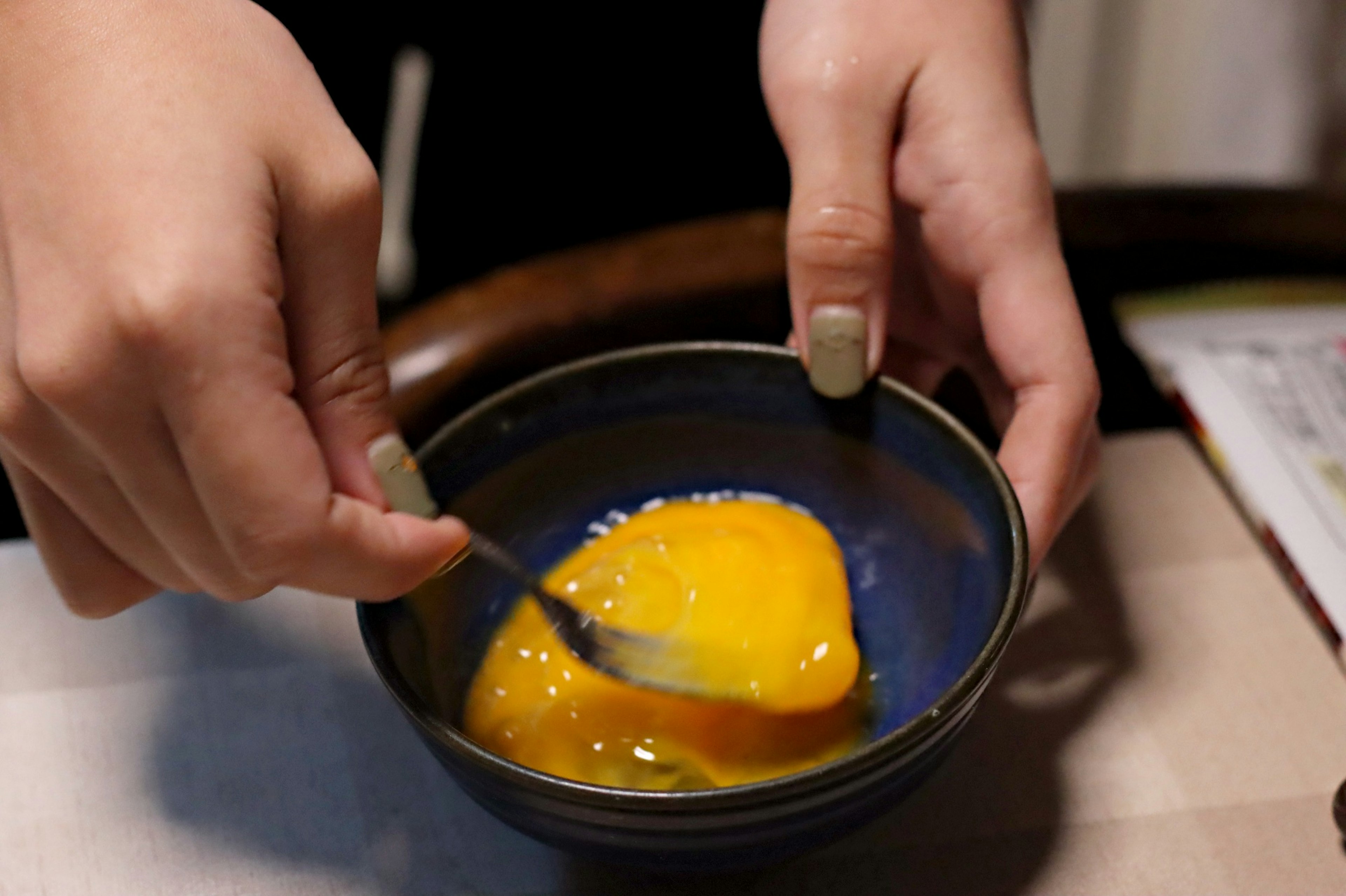 Acercamiento de manos mezclando huevos en un tazón azul con yema y claras